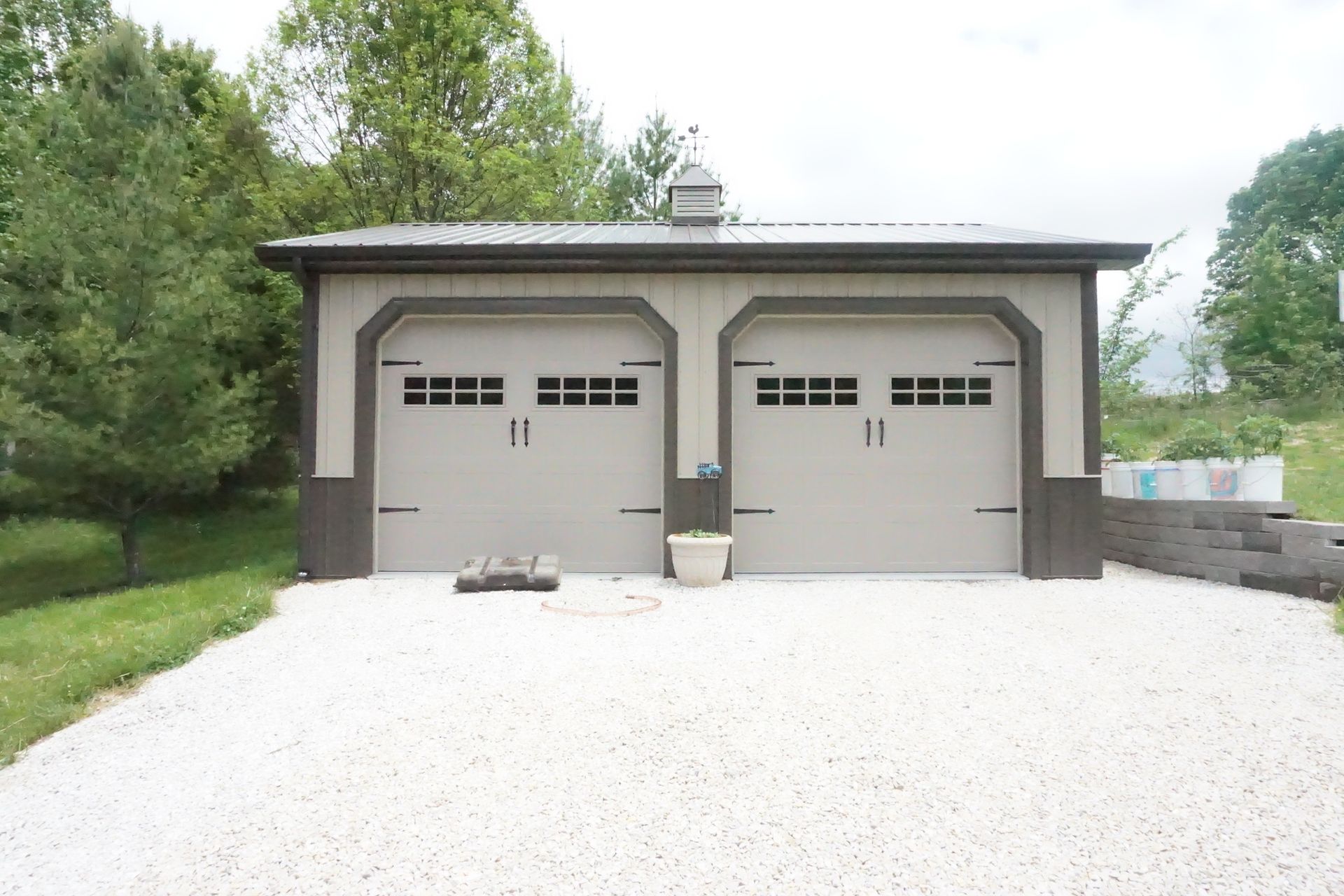 Detached two-car garage with gray doors, white gravel driveway, and trees around it
