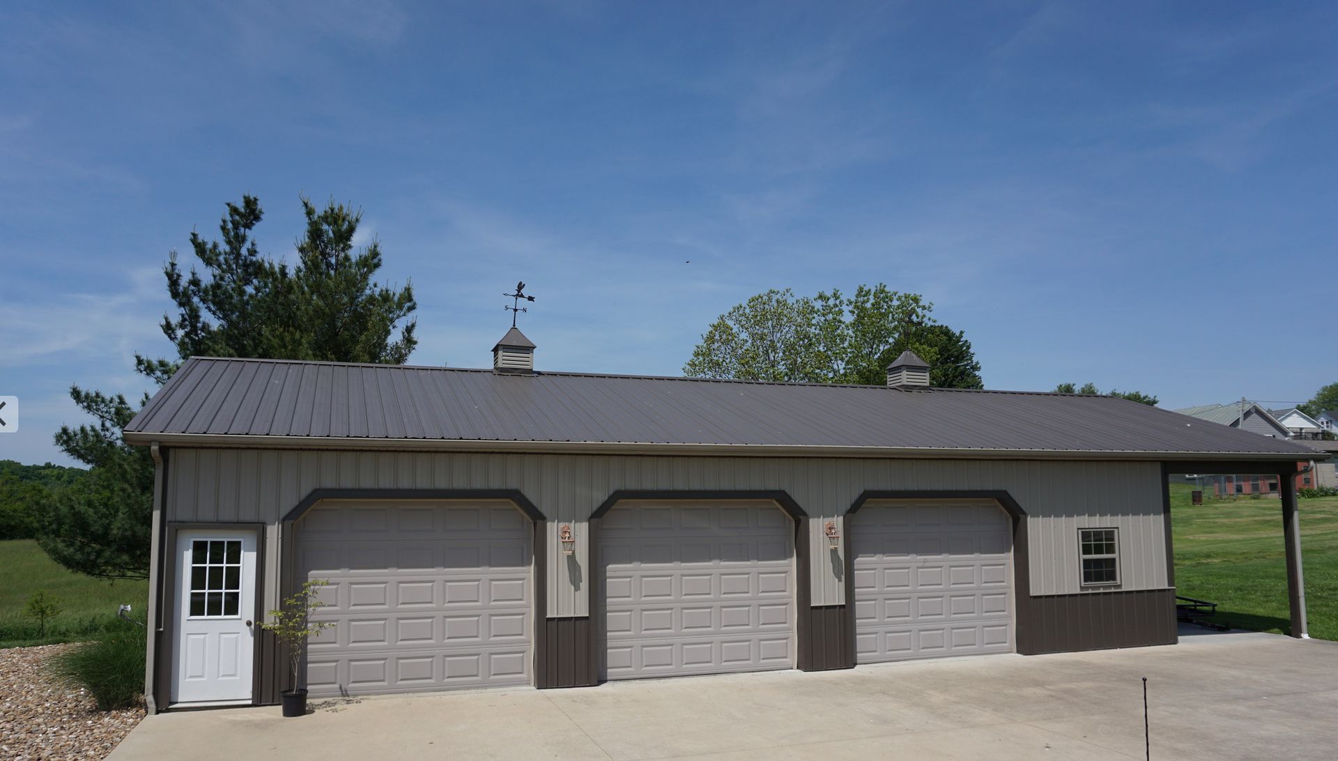Three-bay garage with gray siding and white trim under a blue sky