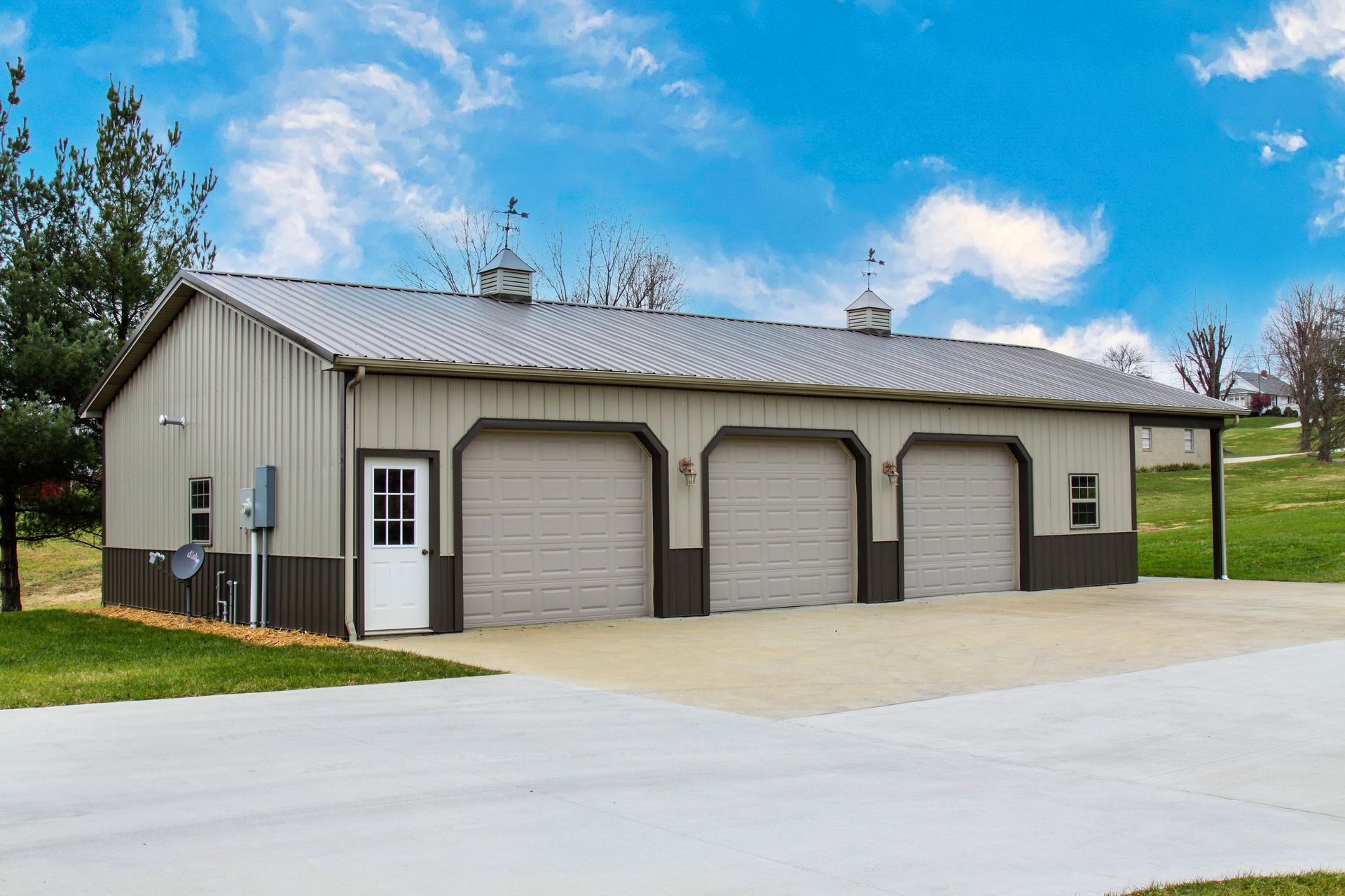 Gray metal garage building with three roll-up doors and a small white side door on a paved lot