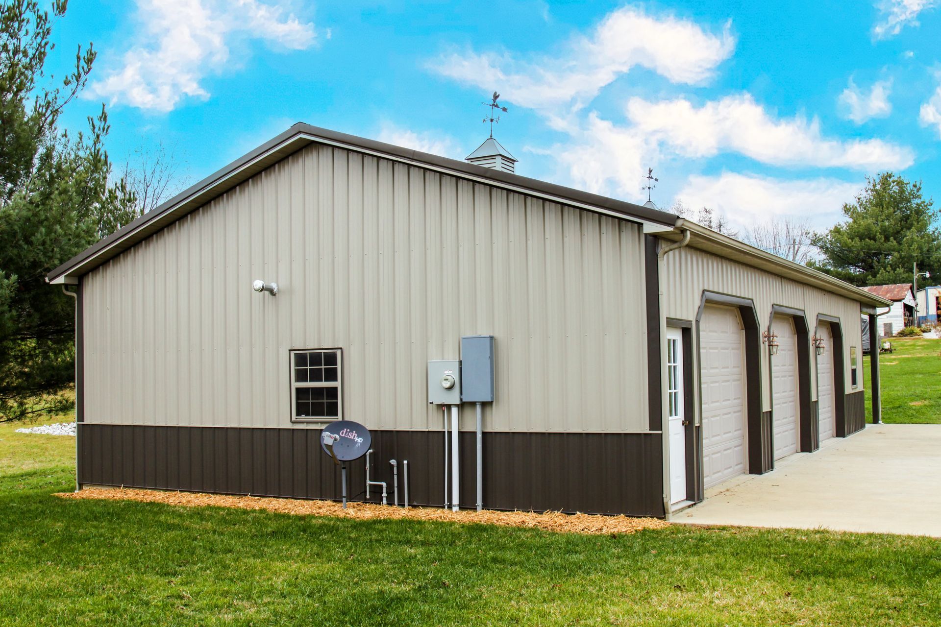 Metal utility building with beige siding, dark base, and garage bays under a blue sky