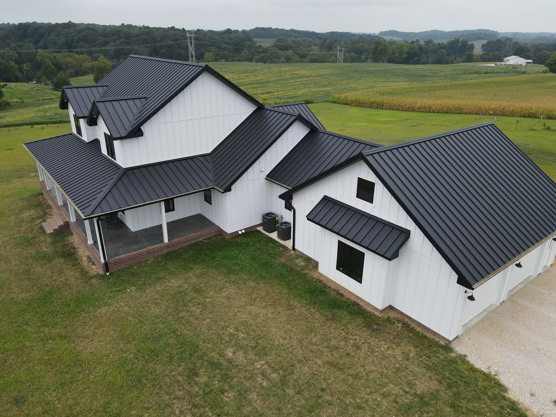 White farmhouse with black metal roofs in a grassy rural field, seen from above