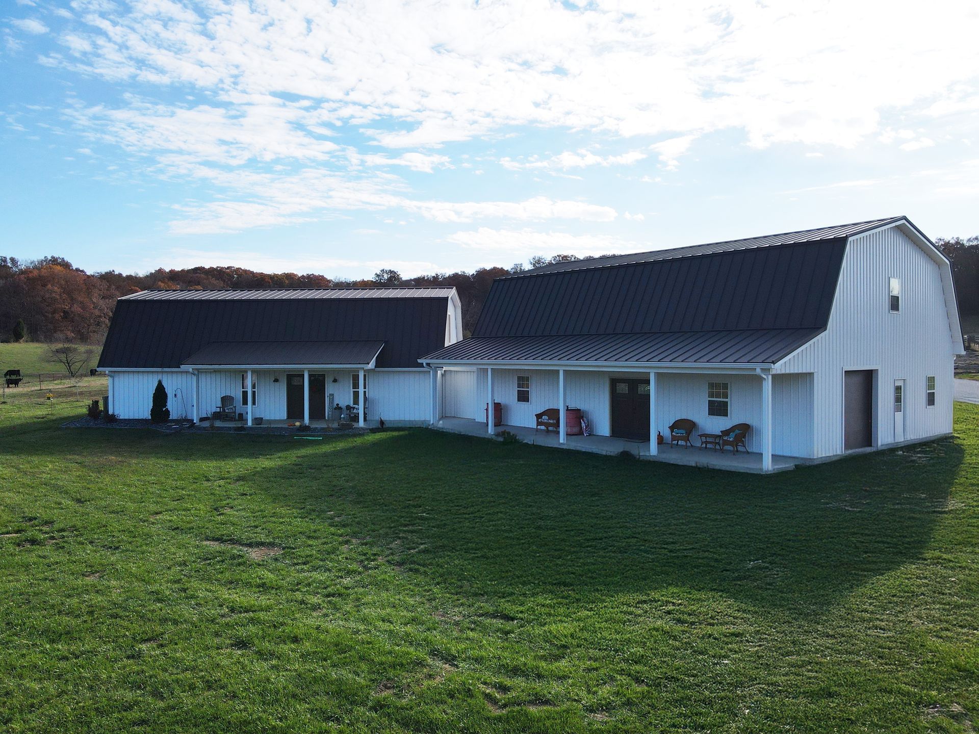 White barn-style house with a dark roof on a grassy lawn under a partly cloudy sky