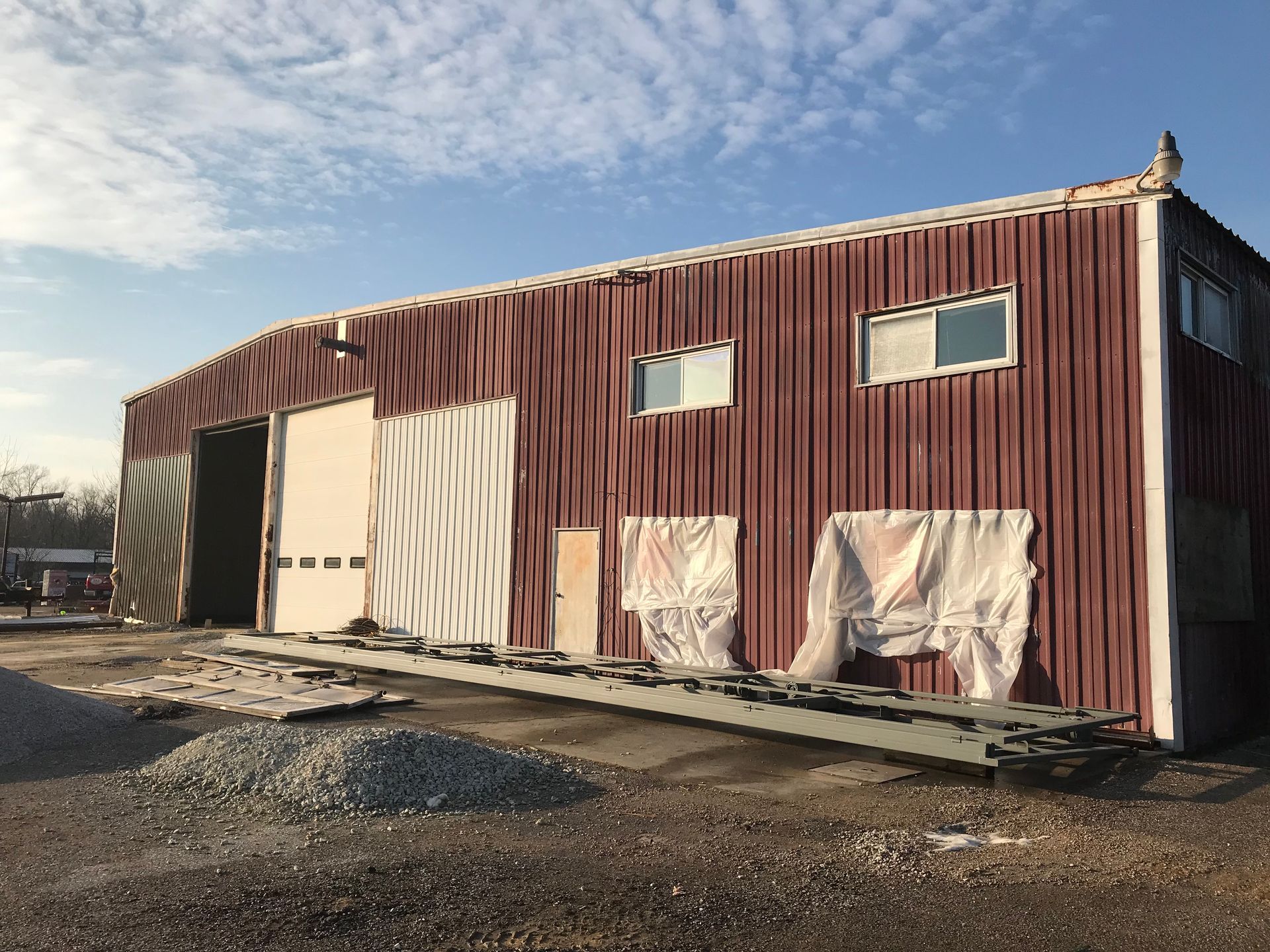 Red corrugated metal warehouse with a large open door in a gravel lot under a blue sky