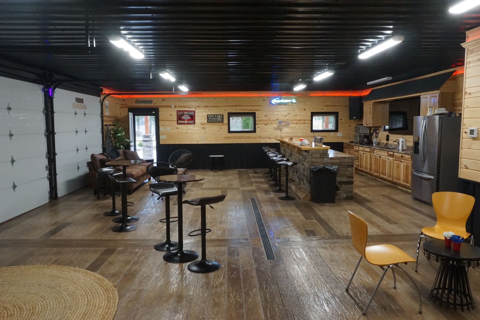 Empty rustic bar interior with wood floors, high tables, stools, and a kitchen area in back