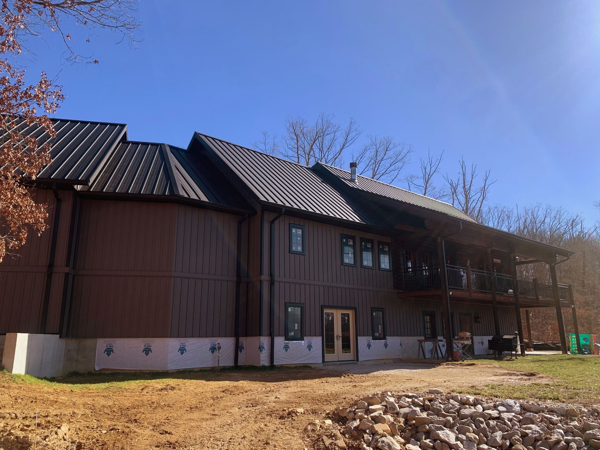 Rustic brown building with a metal roof on a grassy lot under a blue sky