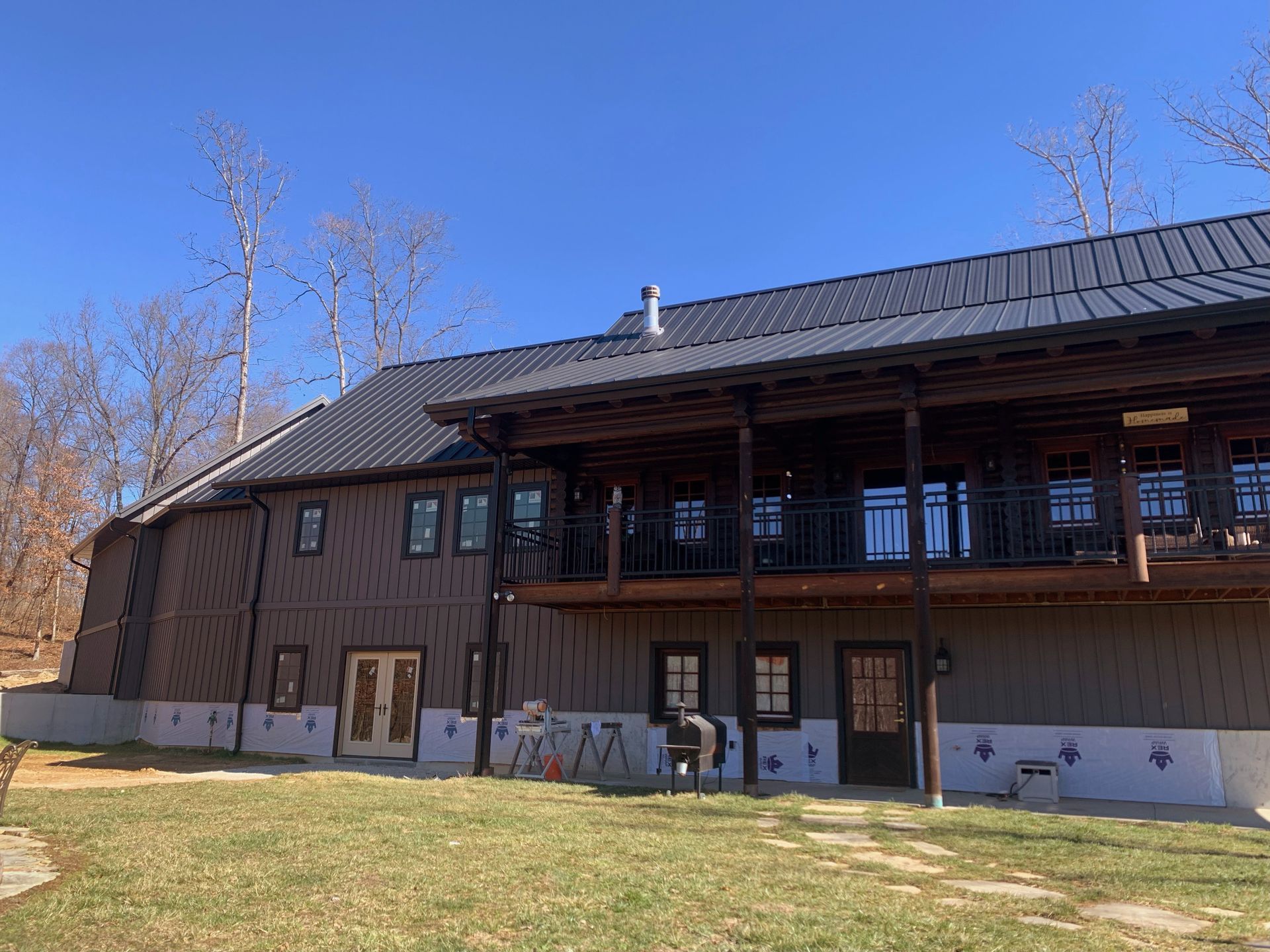 Brown building with a dark roof, wooden balcony, and small windows on a grassy lot under a blue sky