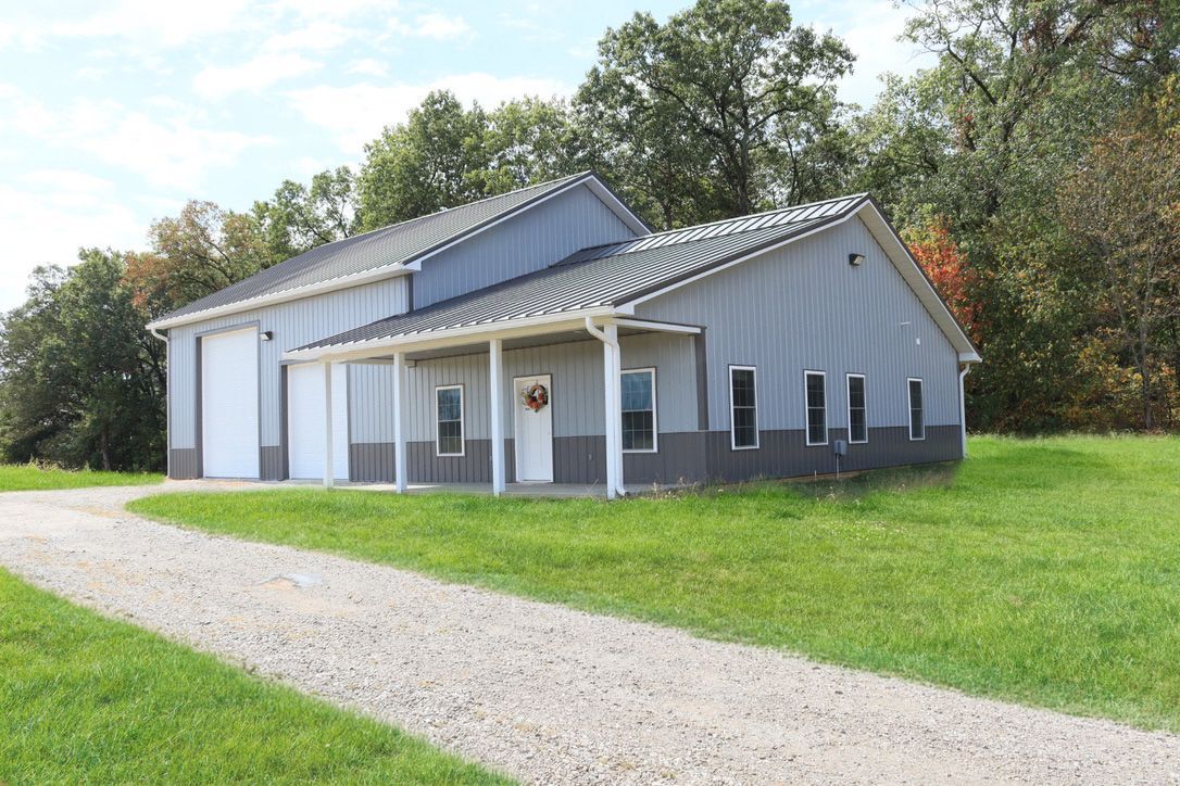 Gray farmhouse-style building with white trim and a gravel path beside a grassy lawn