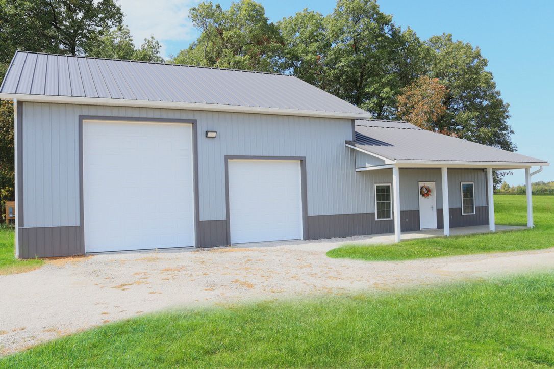 Gray metal barn with large garage doors and a small covered porch beside a grassy yard