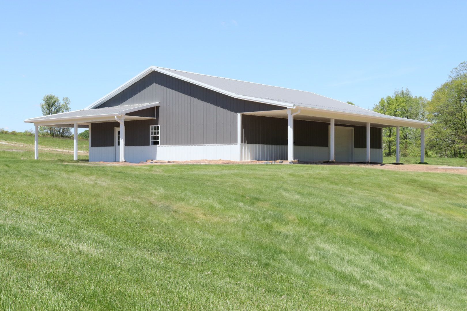 Large gray barn-style building with a metal roof on a grassy hillside under a clear sky