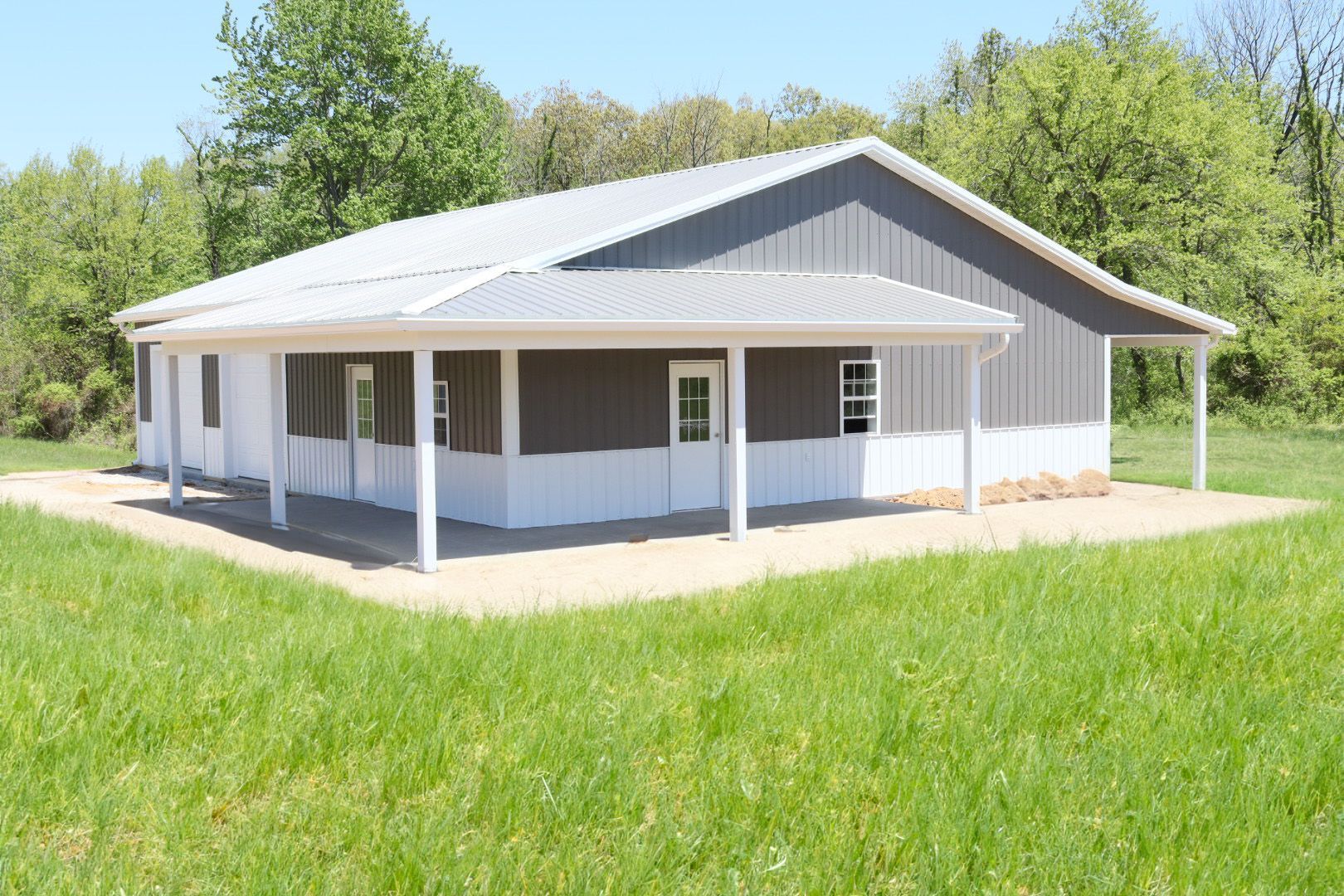 White farmhouse-style building with metal roof and porch, surrounded by green grass and trees