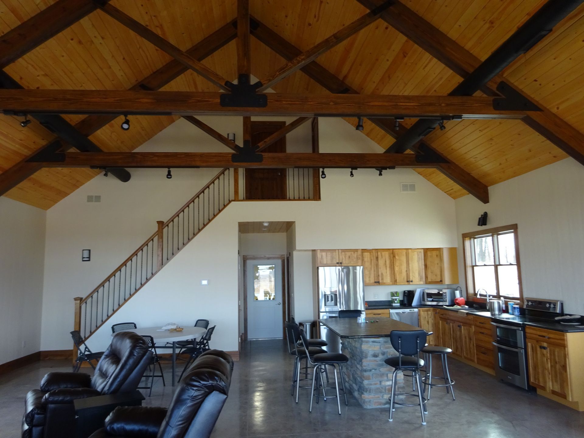 Spacious loft with vaulted wood ceiling, staircase, kitchen, dining area, and black leather sofas