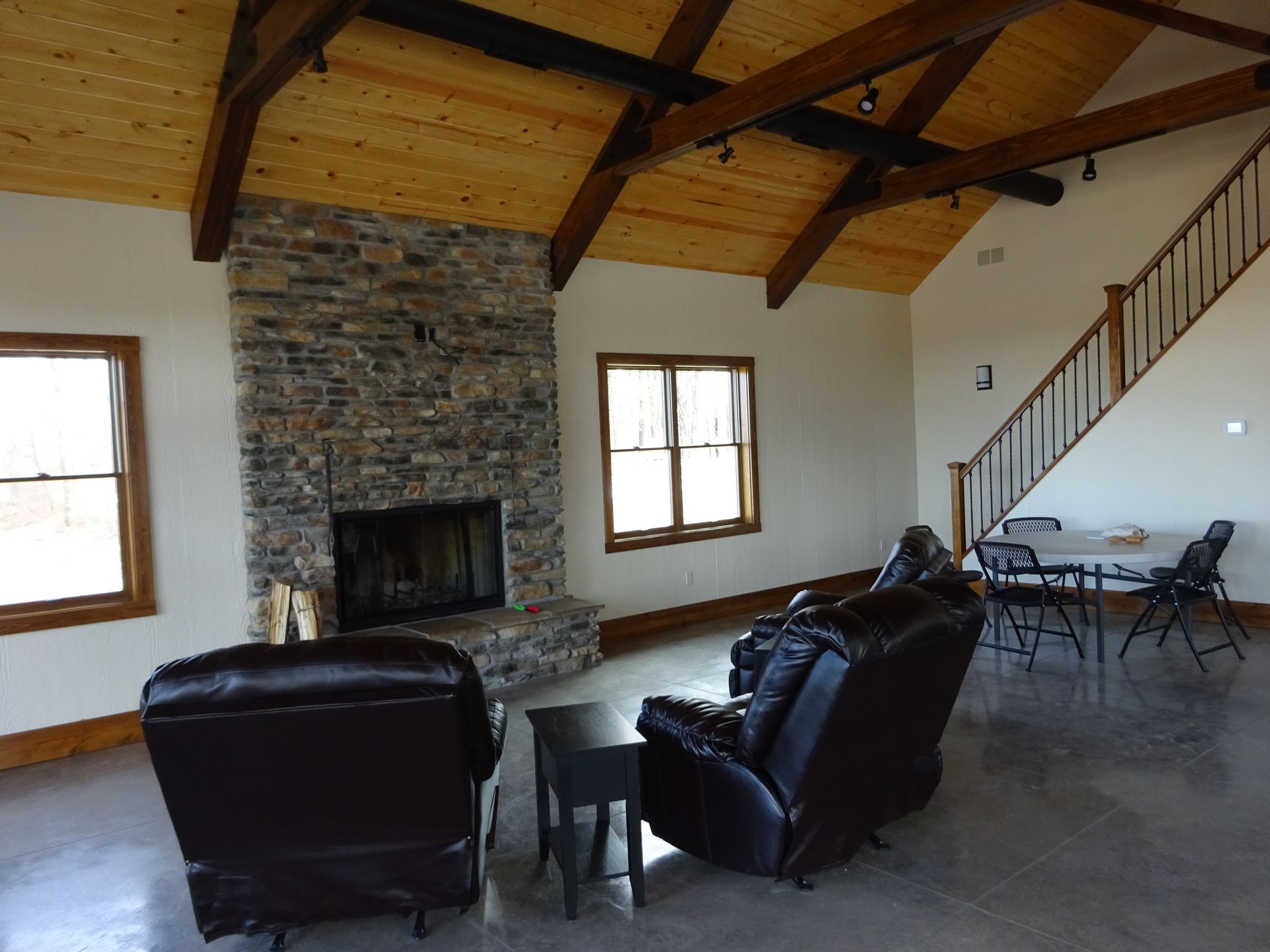 Living room with stone fireplace, leather chairs, exposed wood beams, and staircase.