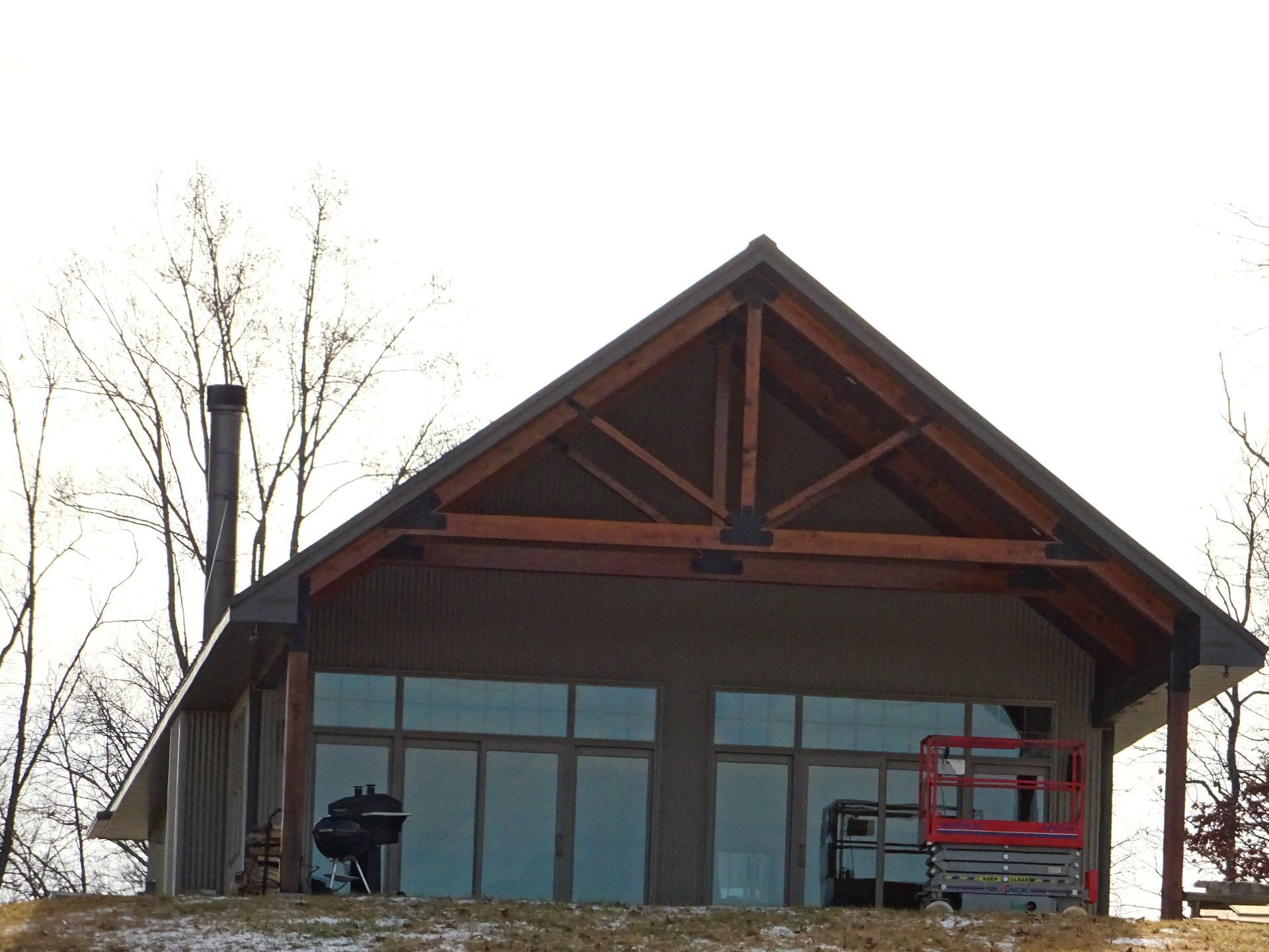 Modern house with large windows and exposed wood trusses, with a red lift parked outside