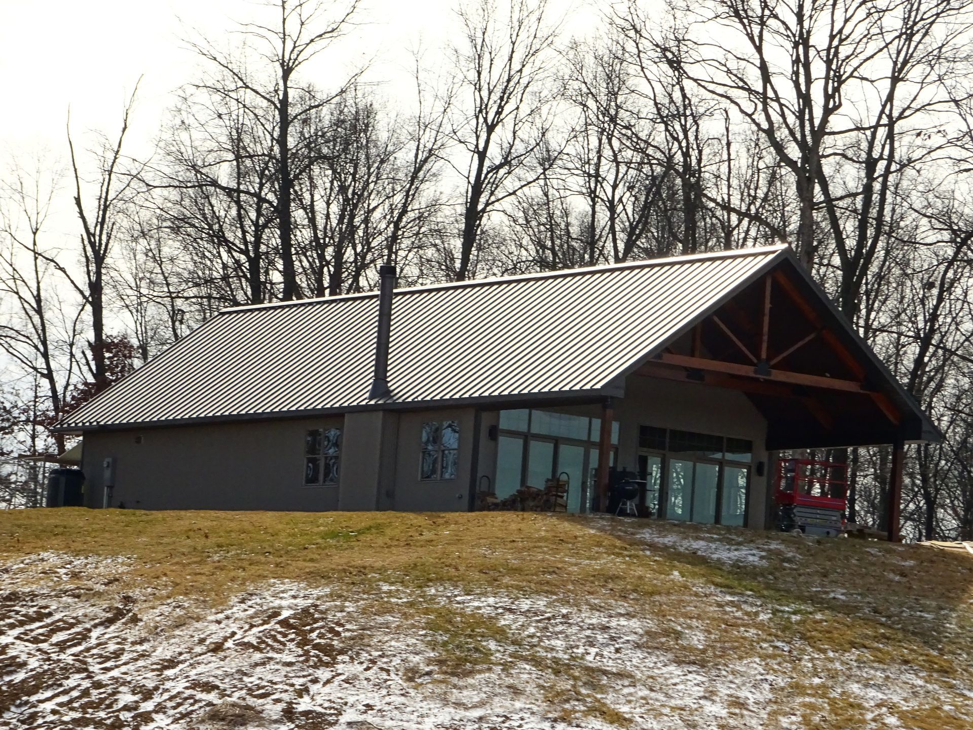 Small pavilion with a metal roof on a snowy hillside, surrounded by leafless trees.
