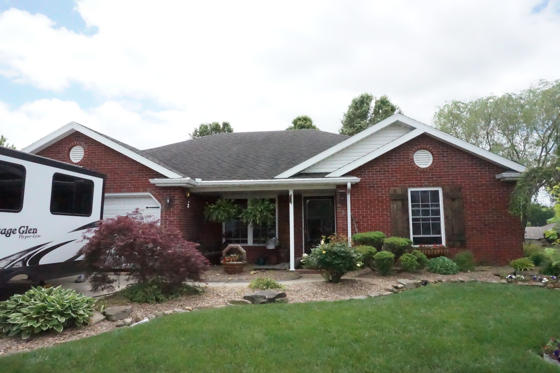 Red brick house with a covered porch, white trim, and a well-kept front lawn and shrubs