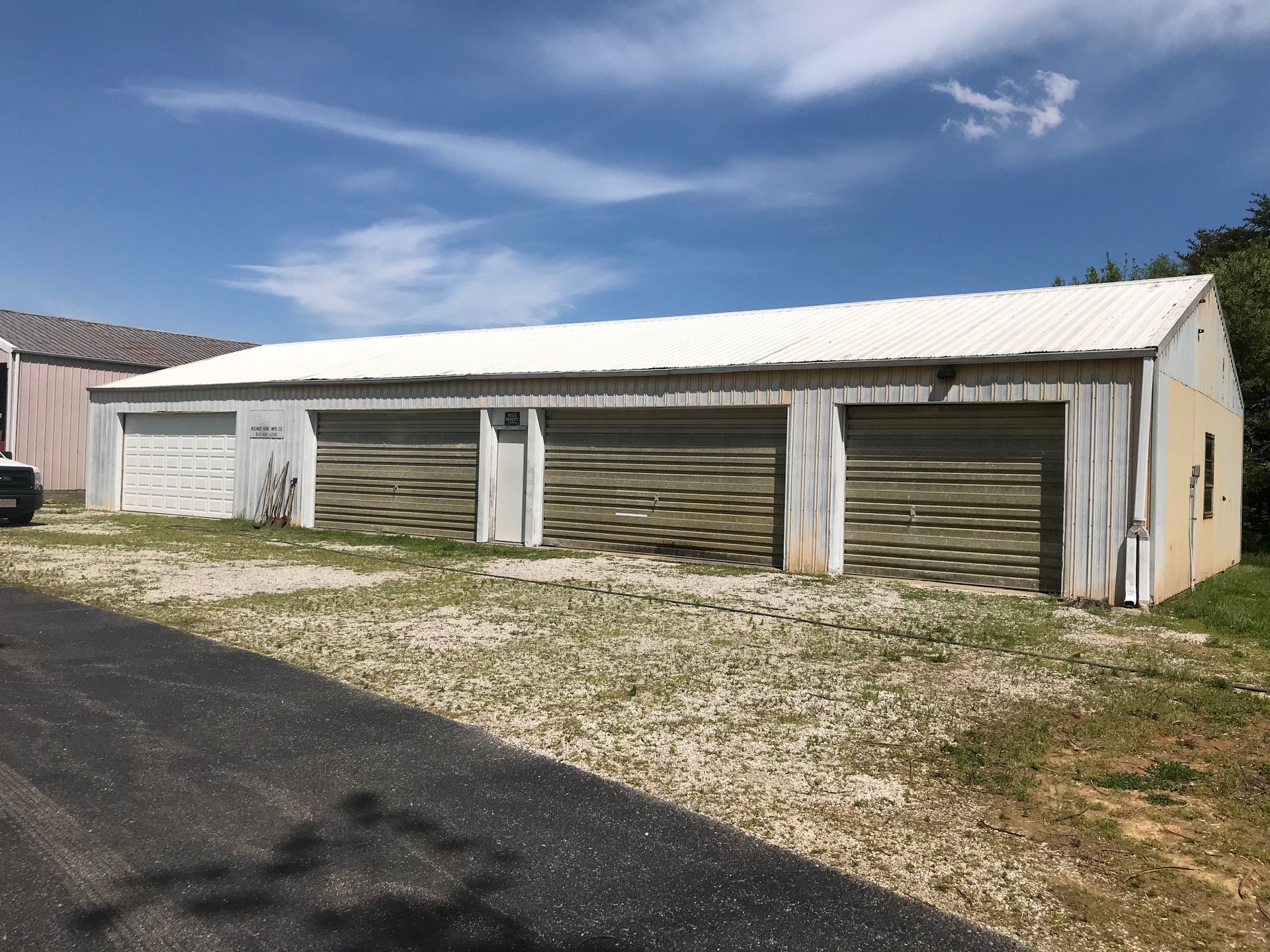 Long white barn with three garage doors under a blue sky on a gravel lot
