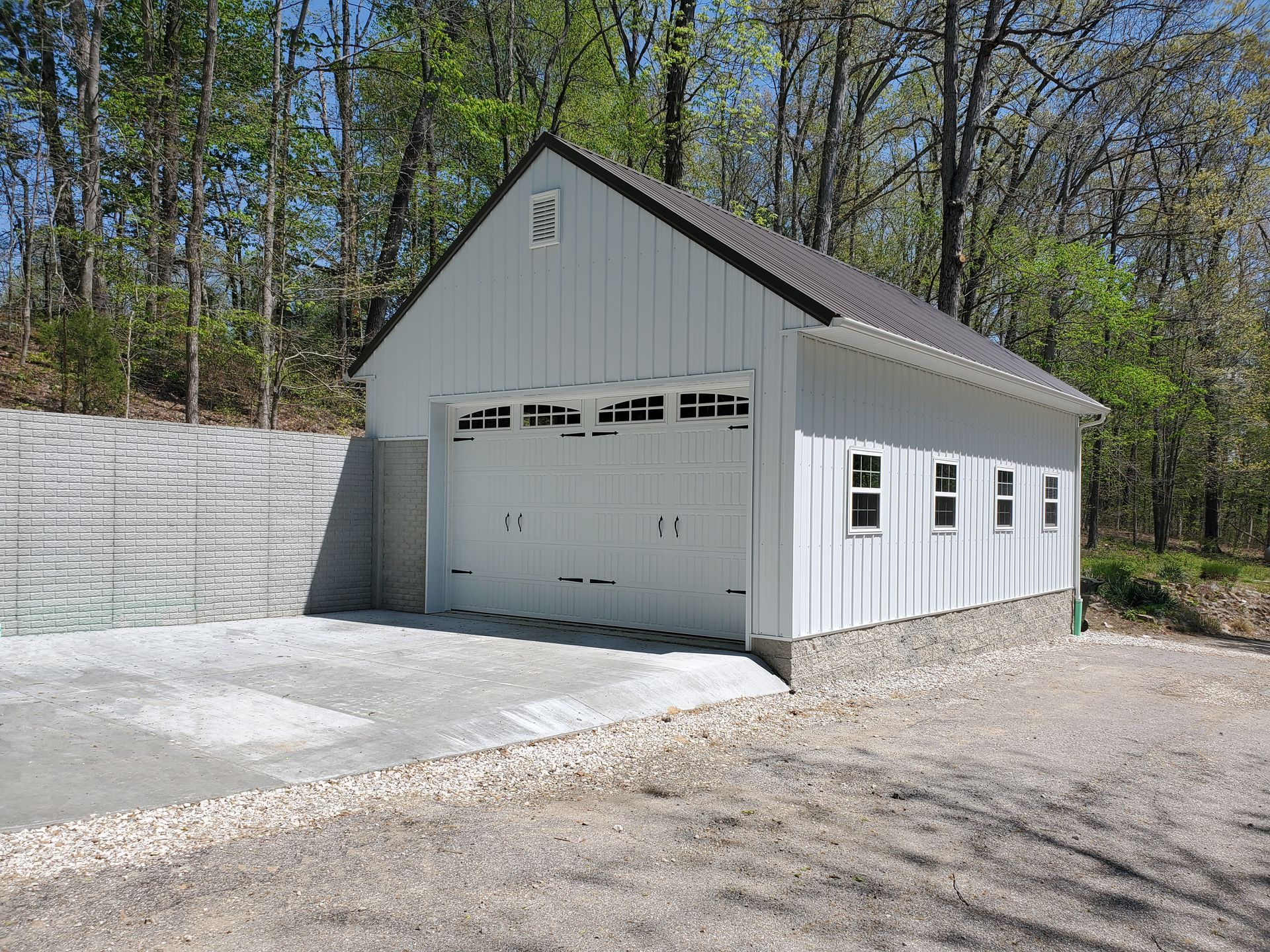 Concrete driveway, foundation, and retaining wall surrounding post frame garage.