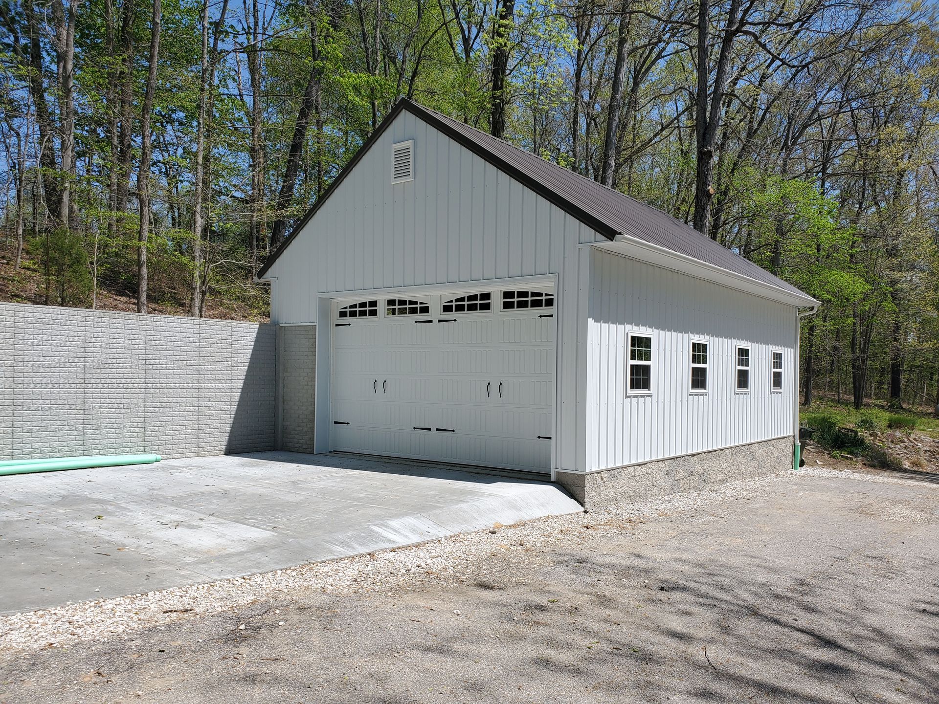 White garage or workshop building with a gabled roof, double doors, and windows on a gravel drive.