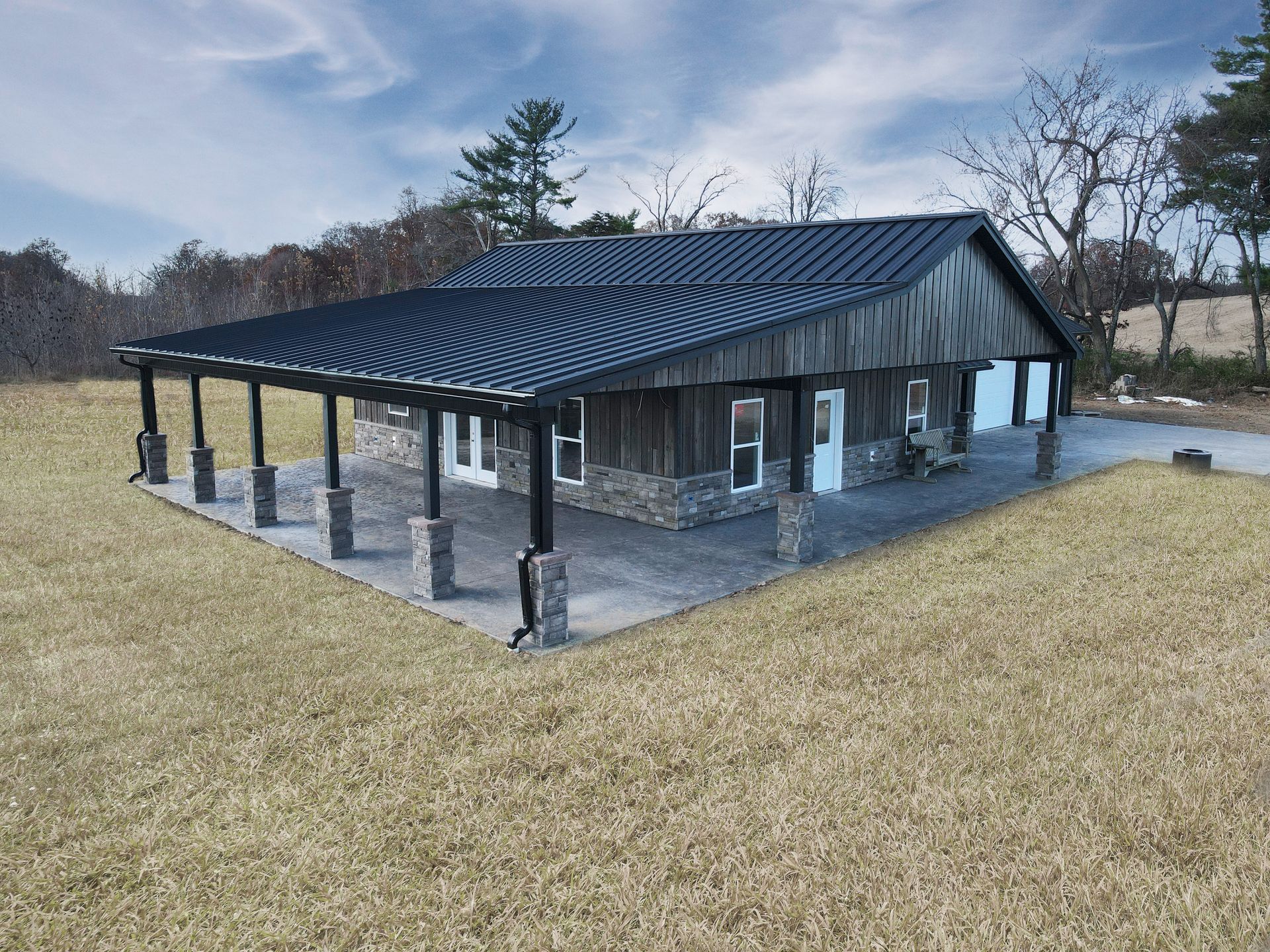 Stone pavilion with a dark metal roof in a grassy field under a cloudy sky