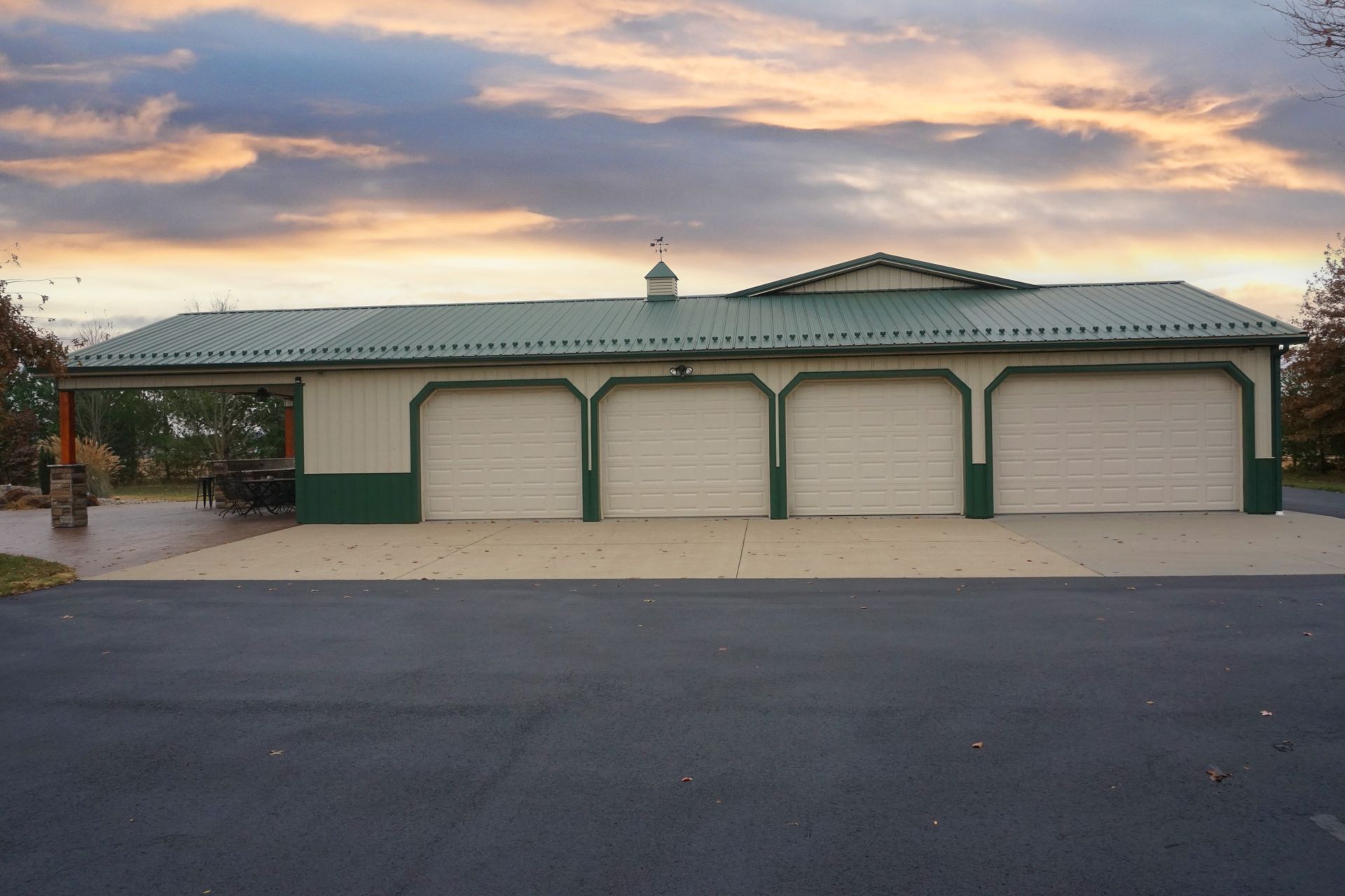 Single-story garage with four white doors and green trim at sunset under a cloudy sky