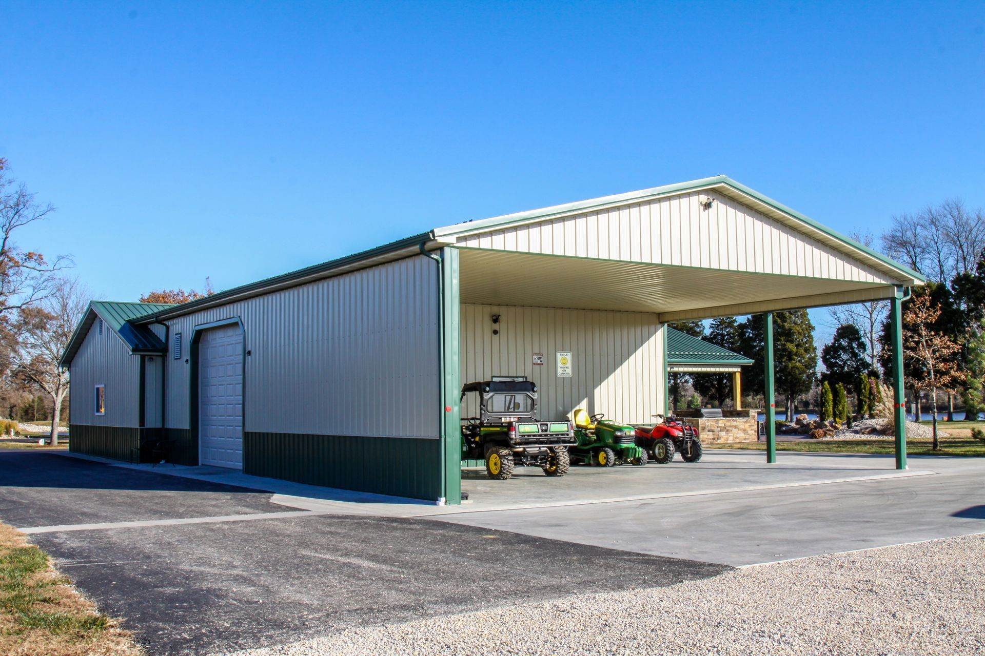 Open-sided metal barn with tractors on a gravel lot under a clear blue sky