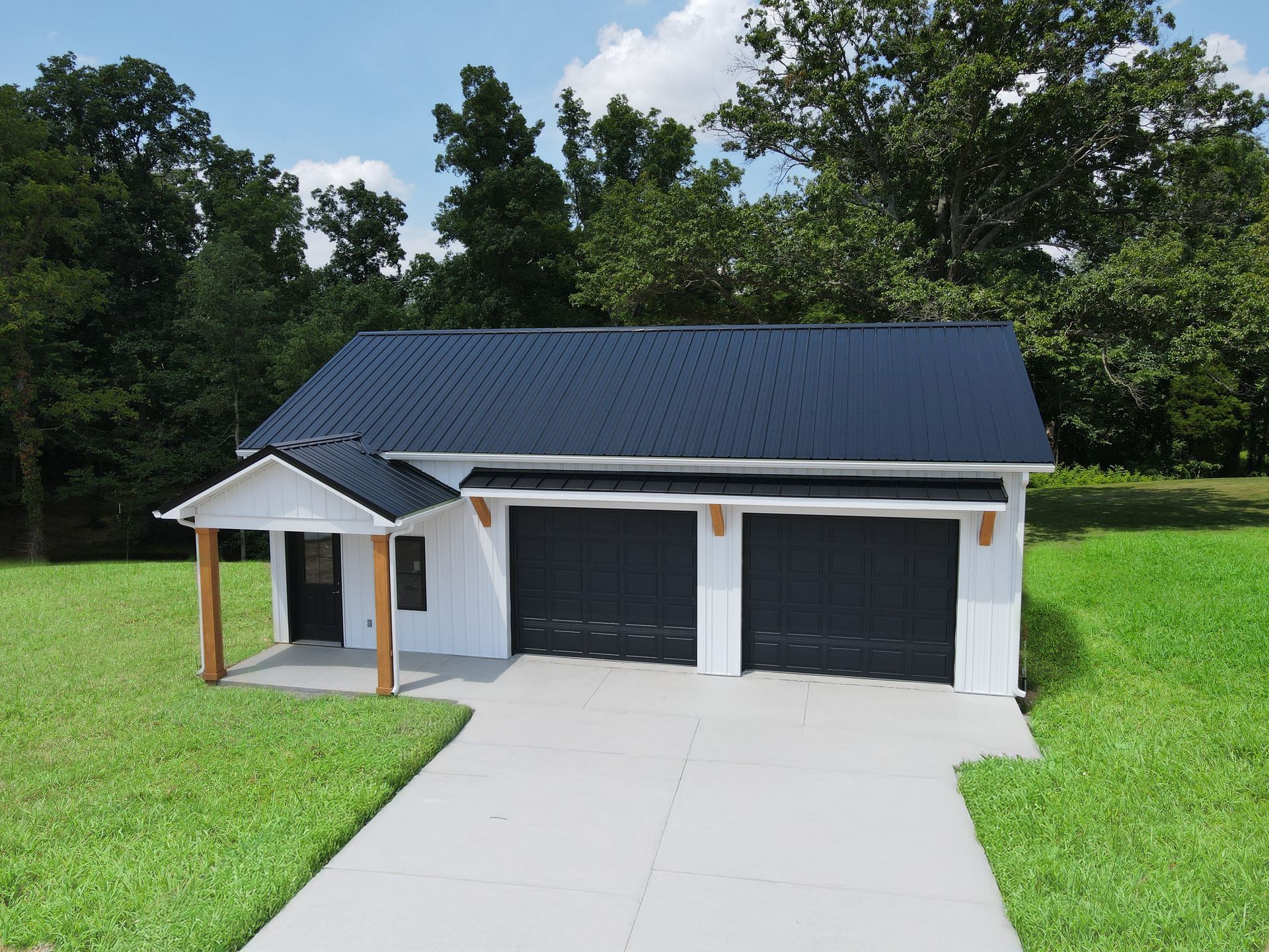 White garage with black roof and double doors beside a concrete driveway and green lawn