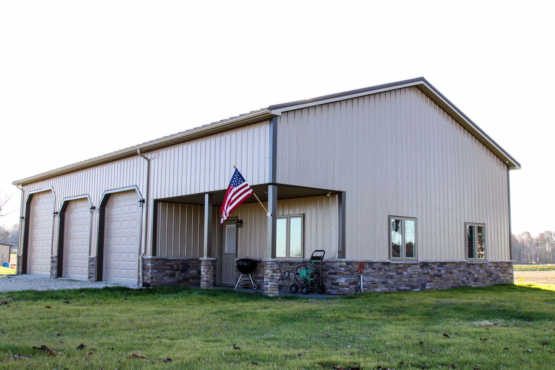 Tan metal building with stone base and an American flag on the front, set on a grassy lot