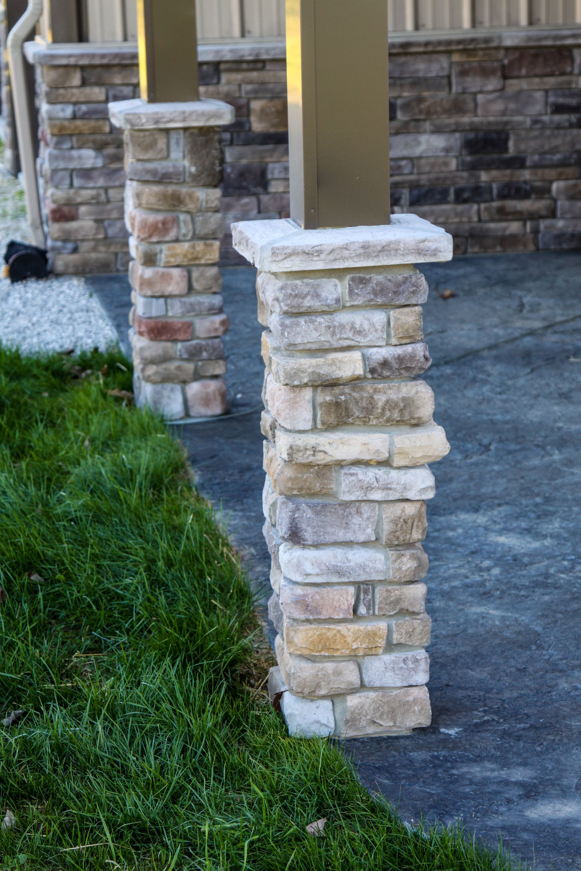 Stone porch columns with beige caps beside a concrete patio and green grass.
