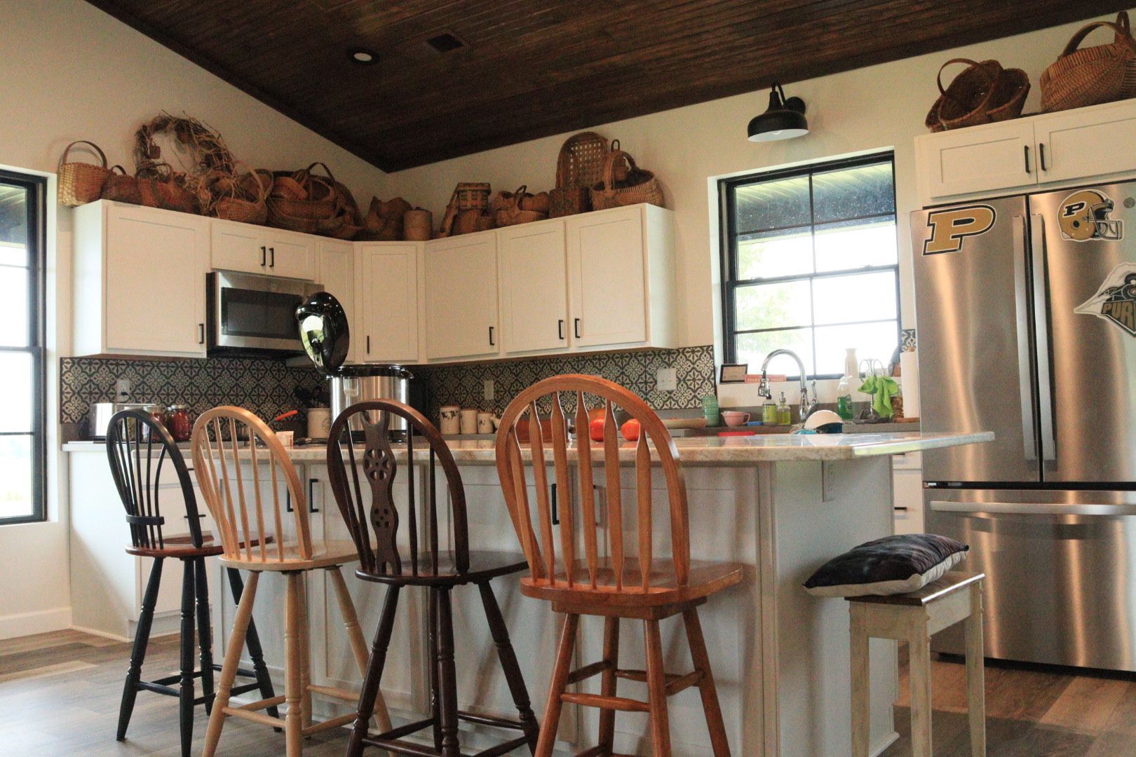 Bright kitchen with white cabinets, stainless fridge, island stools, and large window
