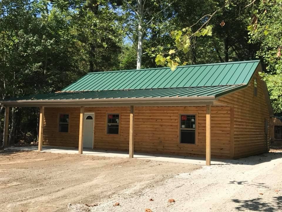Wooden cabin with green metal roof and covered porch in a wooded clearing