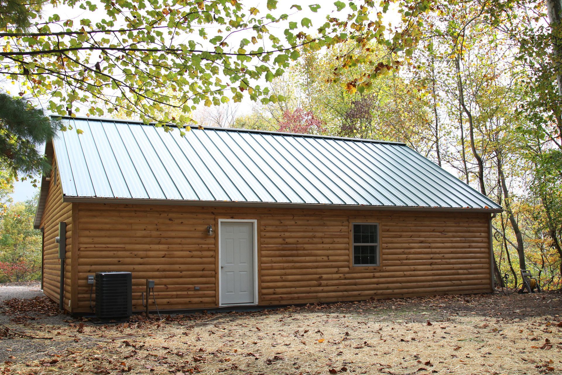Small wooden cabin with a metal roof in a wooded area with fallen leaves