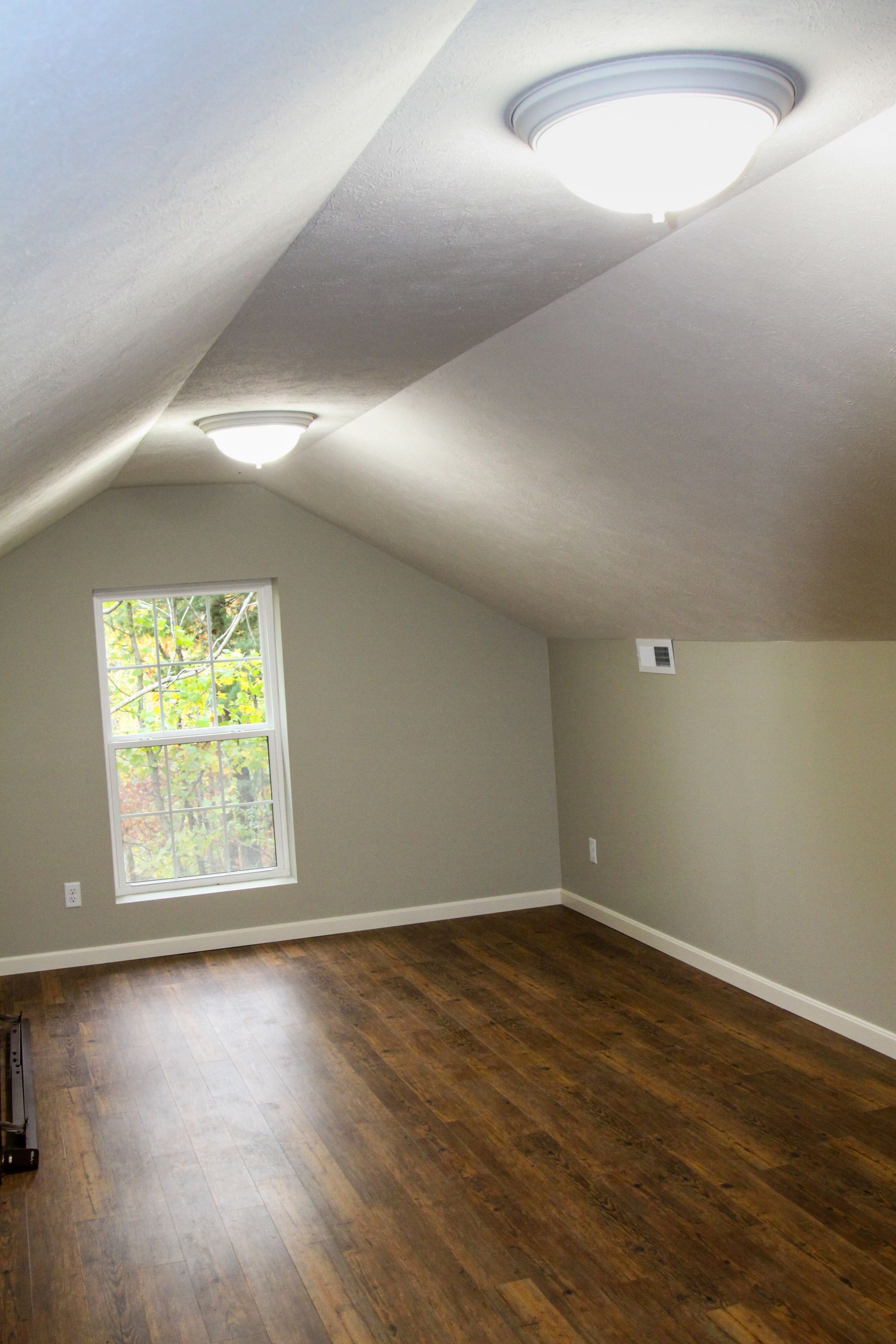 Empty attic-style room with sloped ceiling, two lights, a window, and wood flooring