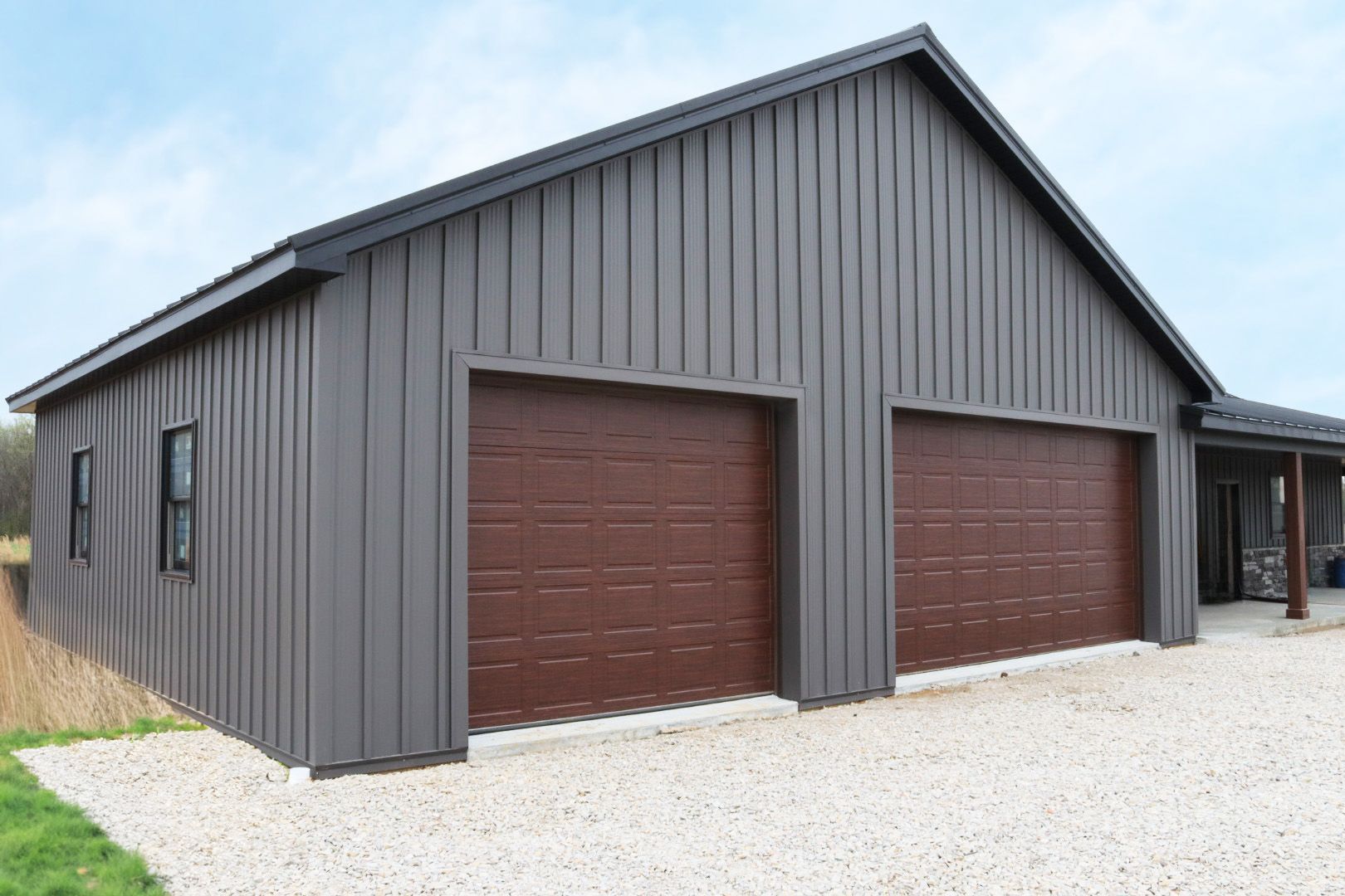 Gray metal garage with two brown doors on a gravel driveway