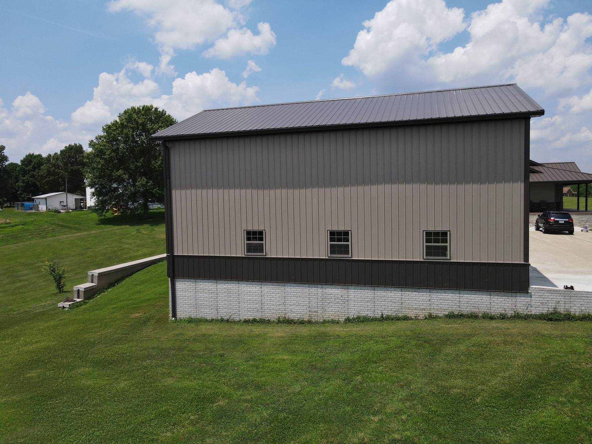 Gray barn with a metal roof on a grassy field under a partly cloudy sky
