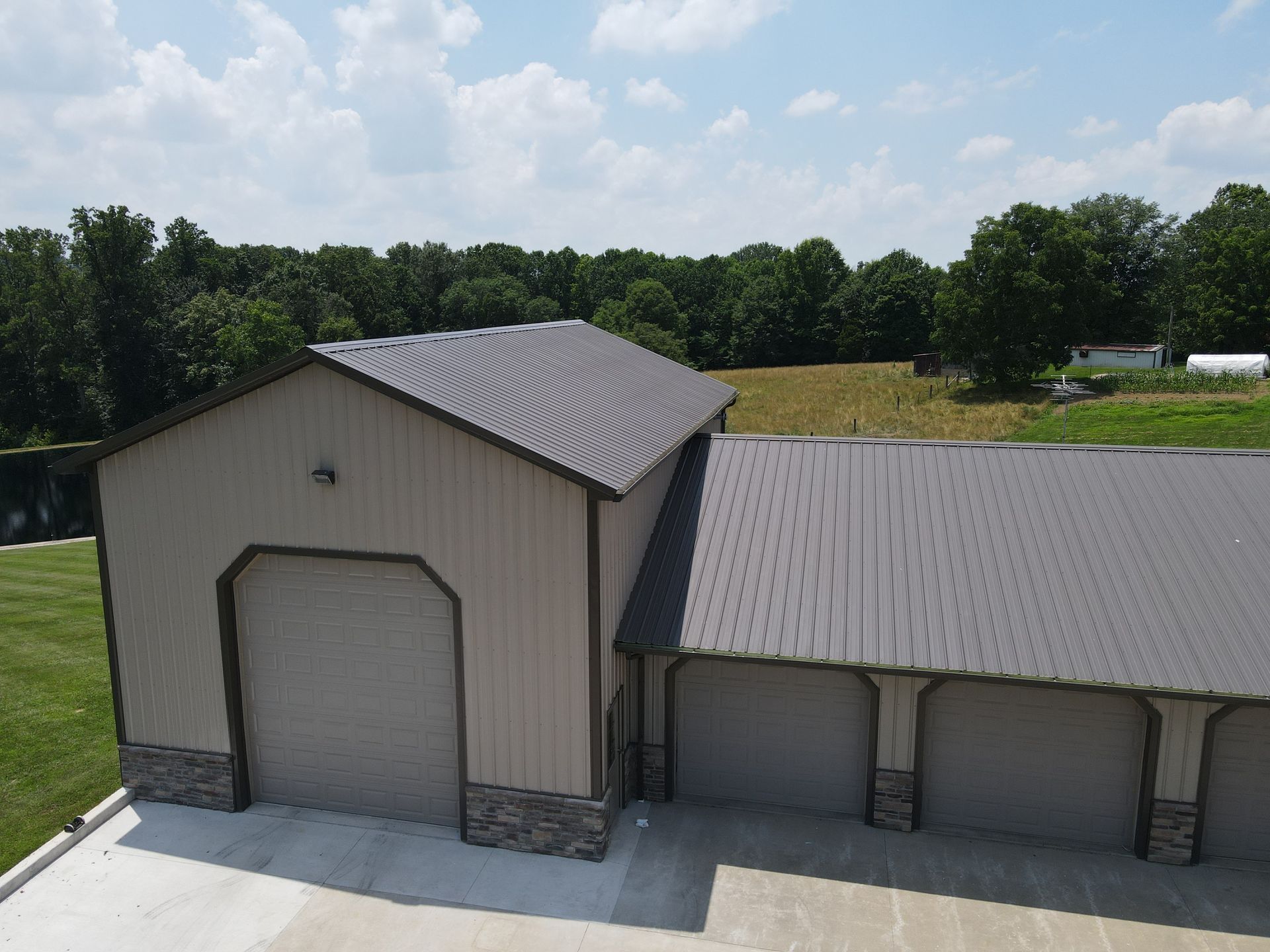 Tan metal-sided barn with gray roof and attached shed on a grassy rural lot