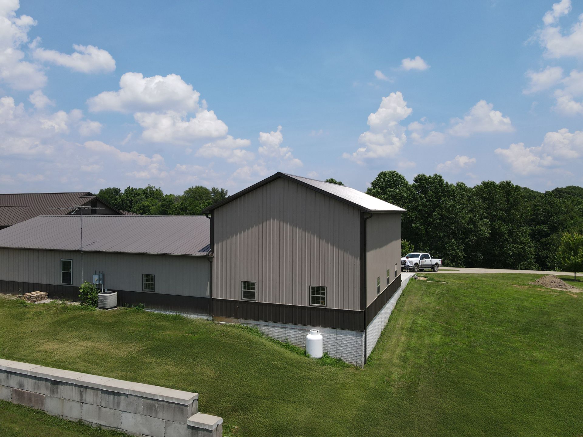 Rural metal building with gray roof beside a grassy slope under a partly cloudy sky
