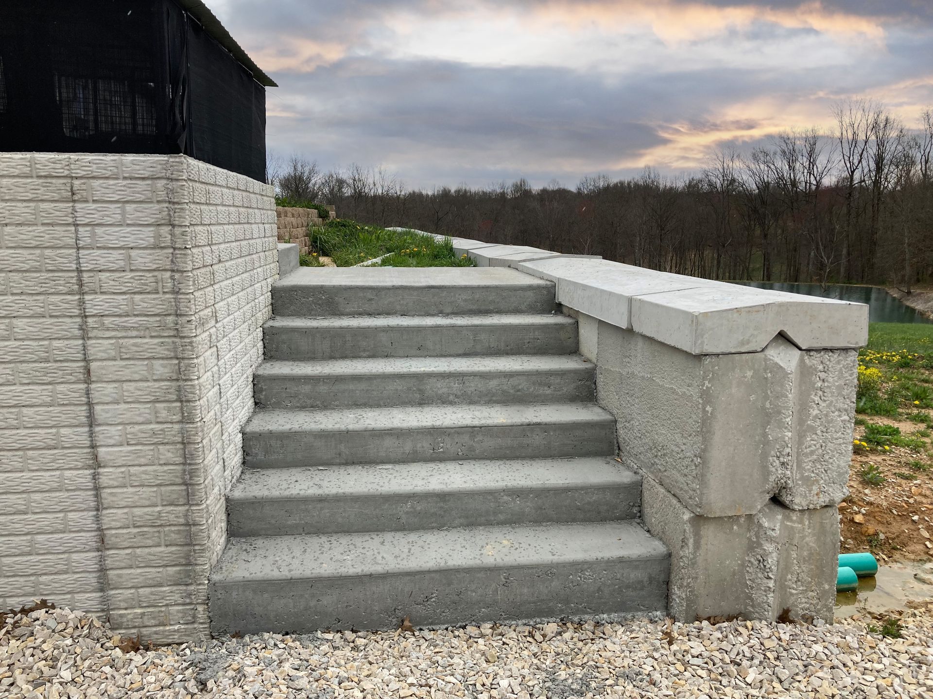 Concrete steps beside a white brick wall, leading to a raised outdoor area under a cloudy sky