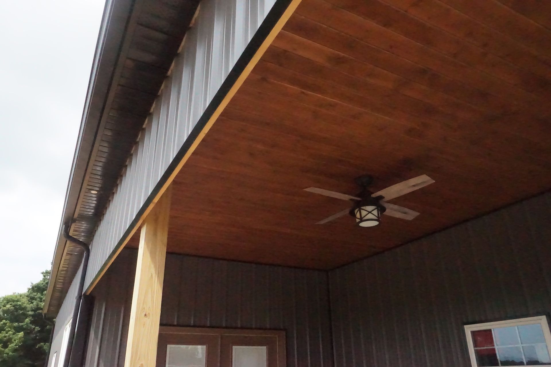 Close-up of a house exterior with wood ceiling, dark siding, and a ceiling fan under the porch roof