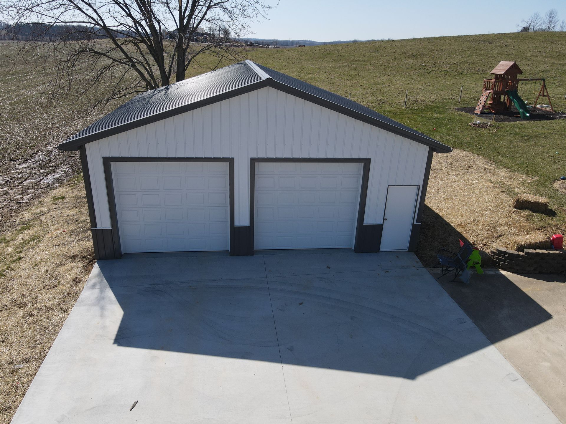 Two-car garage with white doors and a concrete driveway on a grassy hillside.