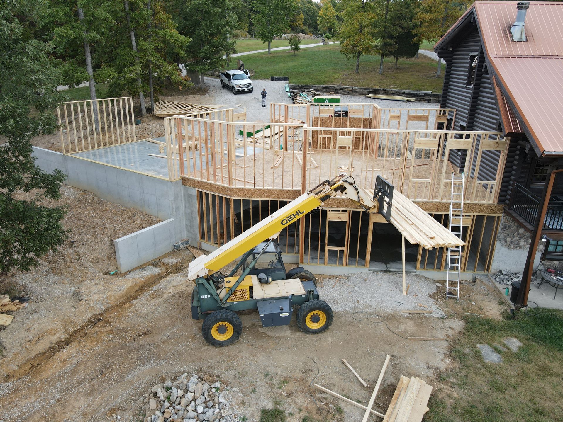 Construction site with a yellow telescopic forklift beside a partially built wooden house foundation and framing