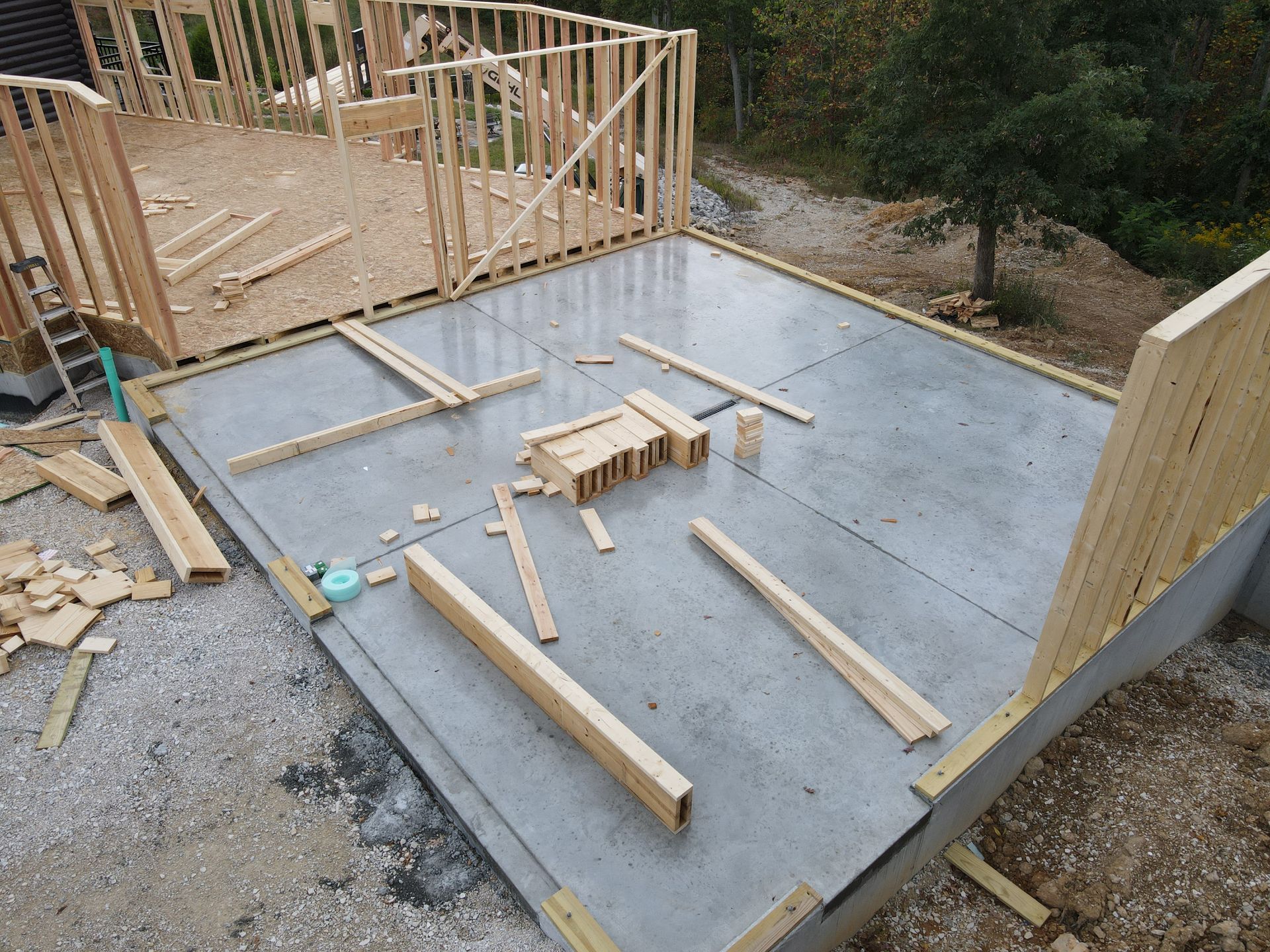 Wood-framed house under construction on a concrete slab with scattered lumber and foundation walls.
