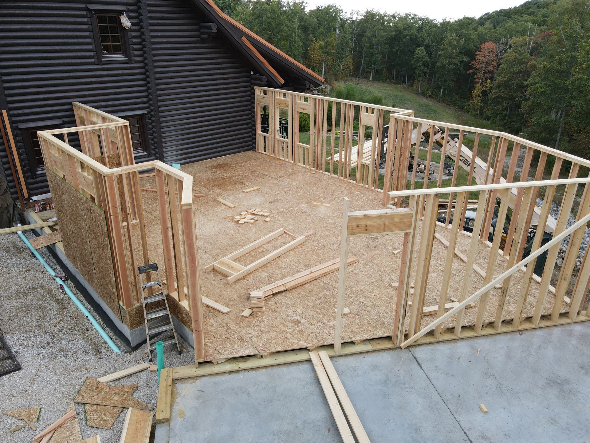 Partially built wooden deck frame beside a cabin, with exposed studs and plywood floor.