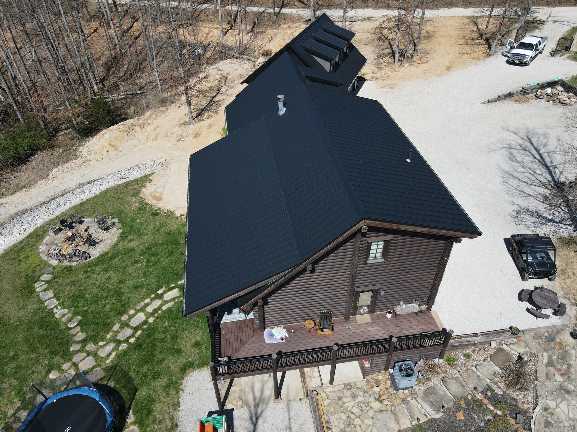 Aerial view of a rustic cabin with a dark roof, surrounded by gravel driveways and bare trees.