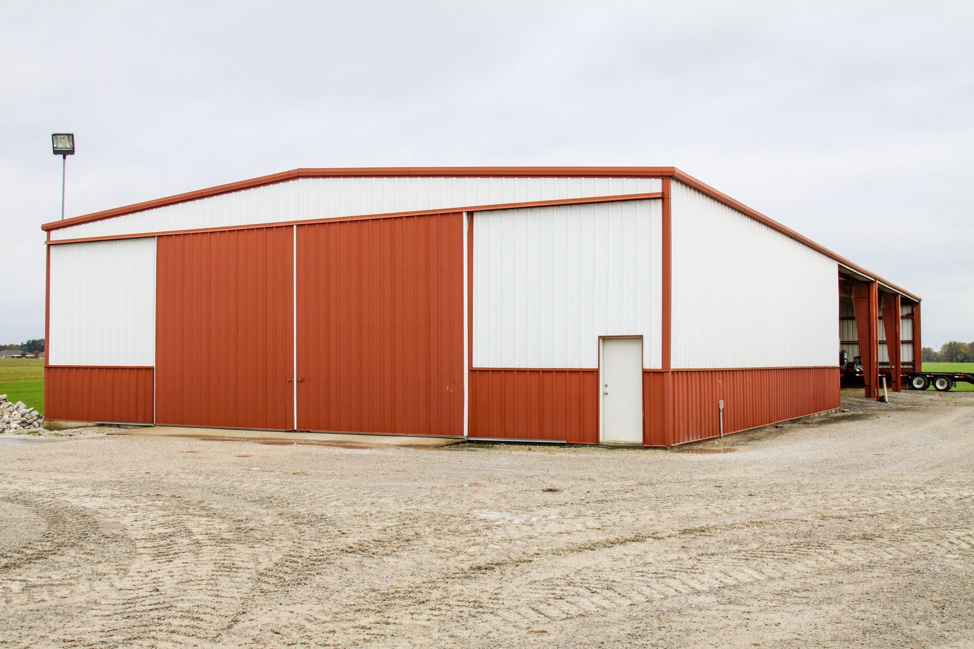 Red and white metal warehouse on a gravel lot under an overcast sky