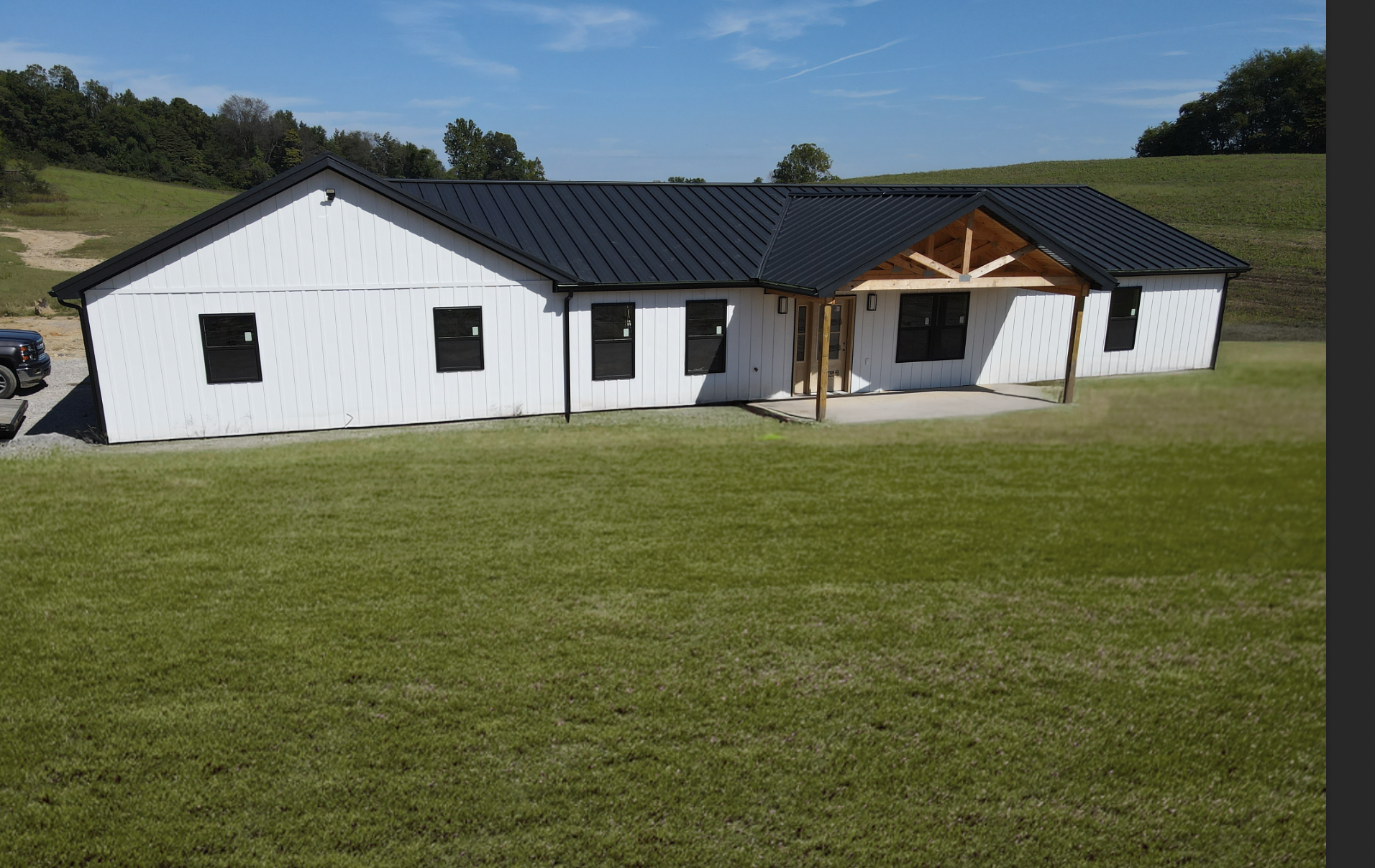 White single-story house with a black roof and covered porch on a large grassy lawn