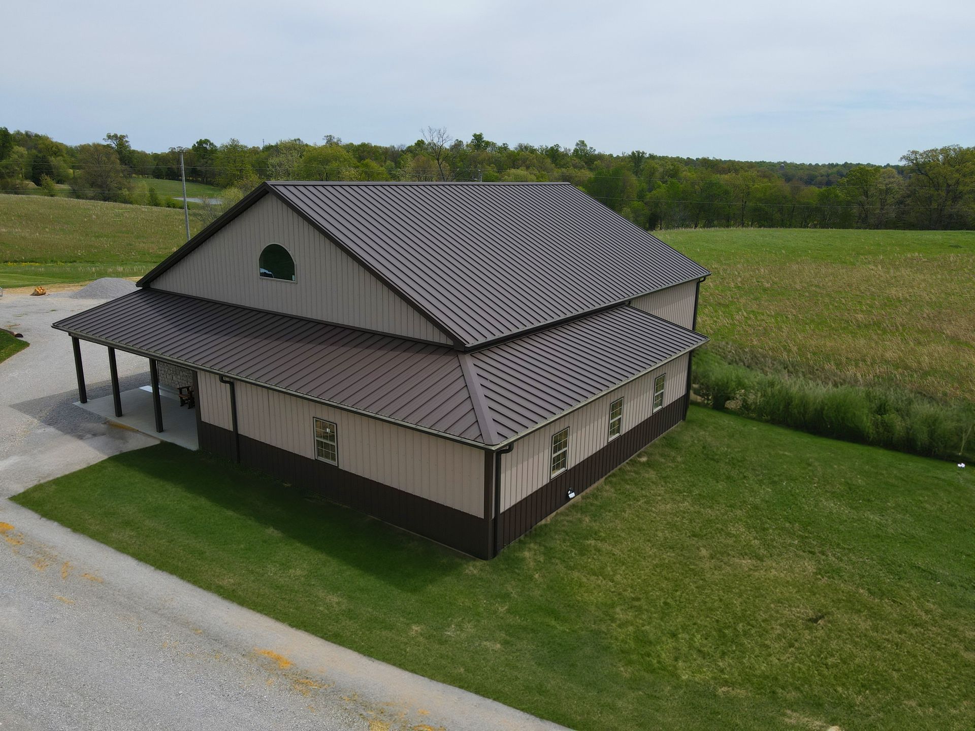 Small rural barn with a gray metal roof beside a road and grassy field under an overcast sky