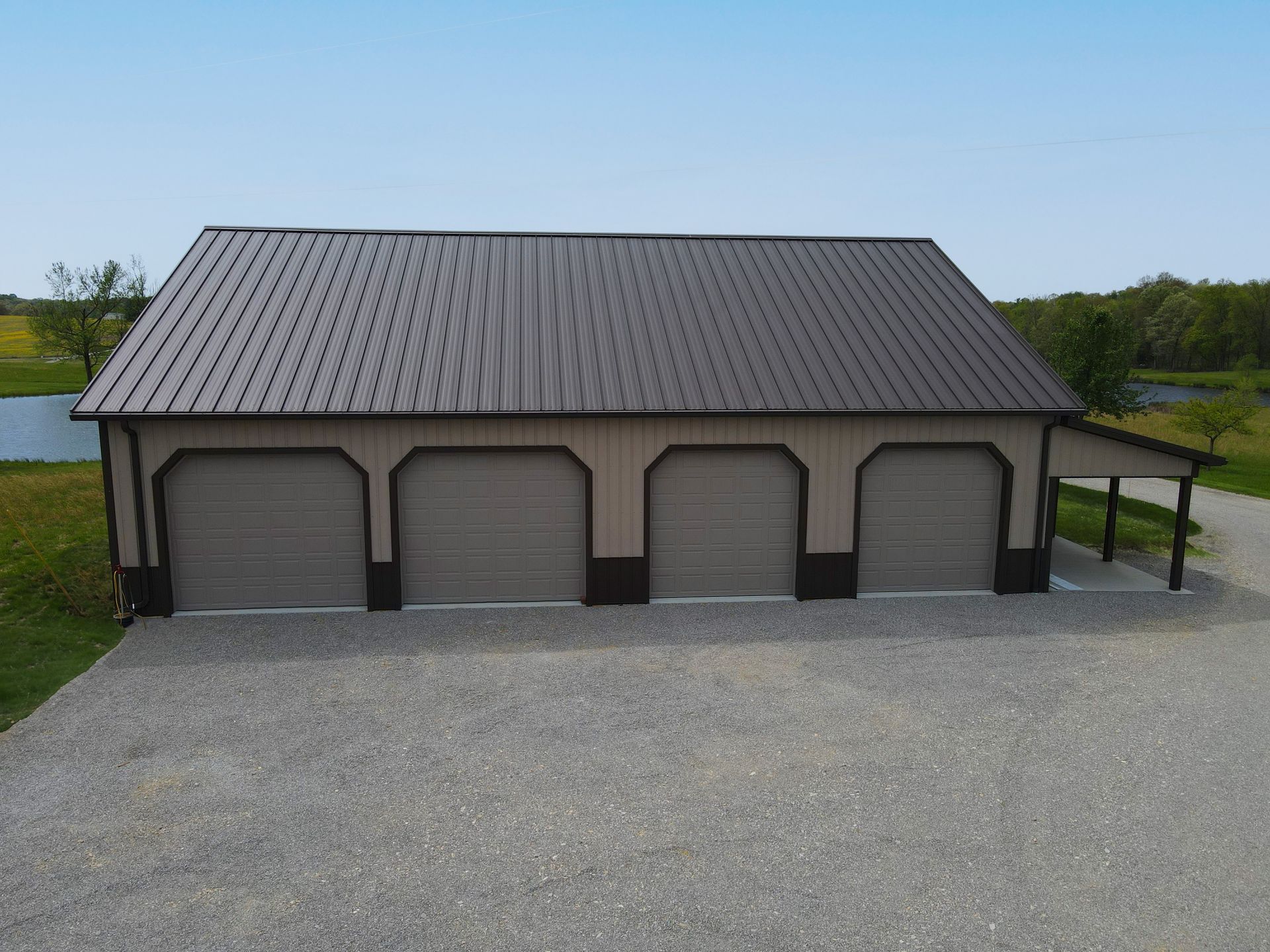 Large gray garage with four arched doors and a metal roof on a gravel lot under a clear sky
