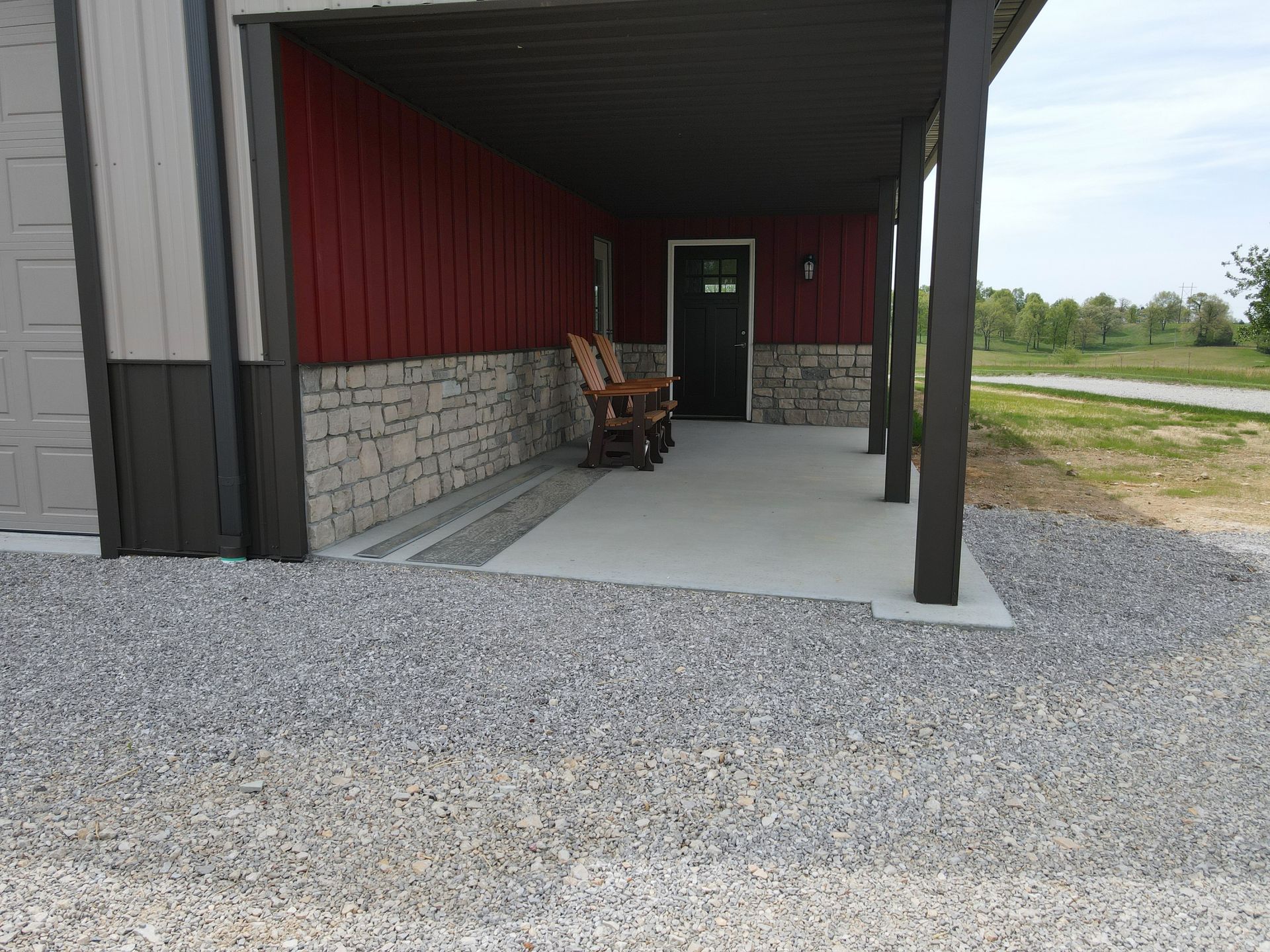 Dark red metal siding with stone wainscot accenting on porch. Concrete drain in concrete prevents water pooling.