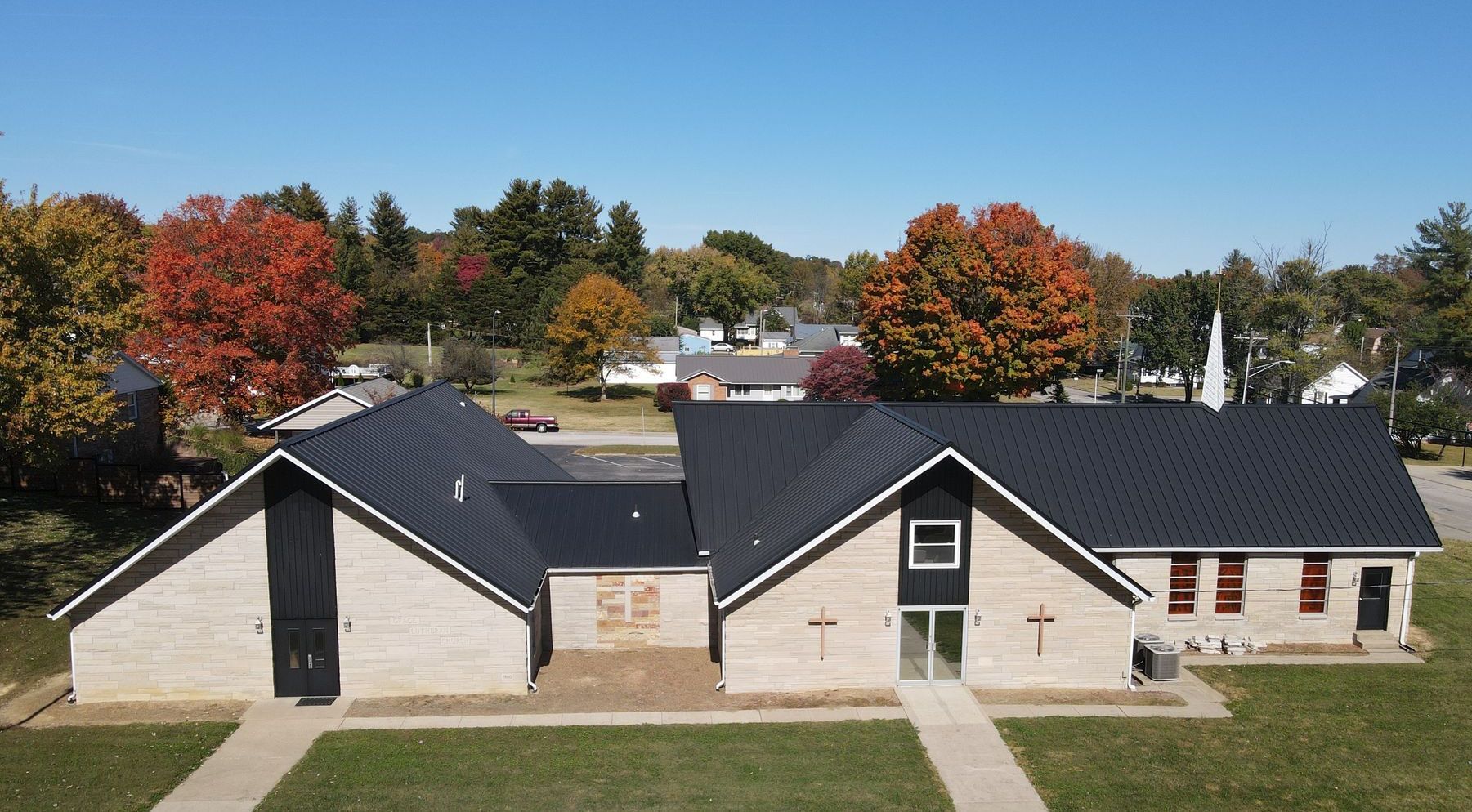 Single-story beige house with dark roof and autumn trees in front yard