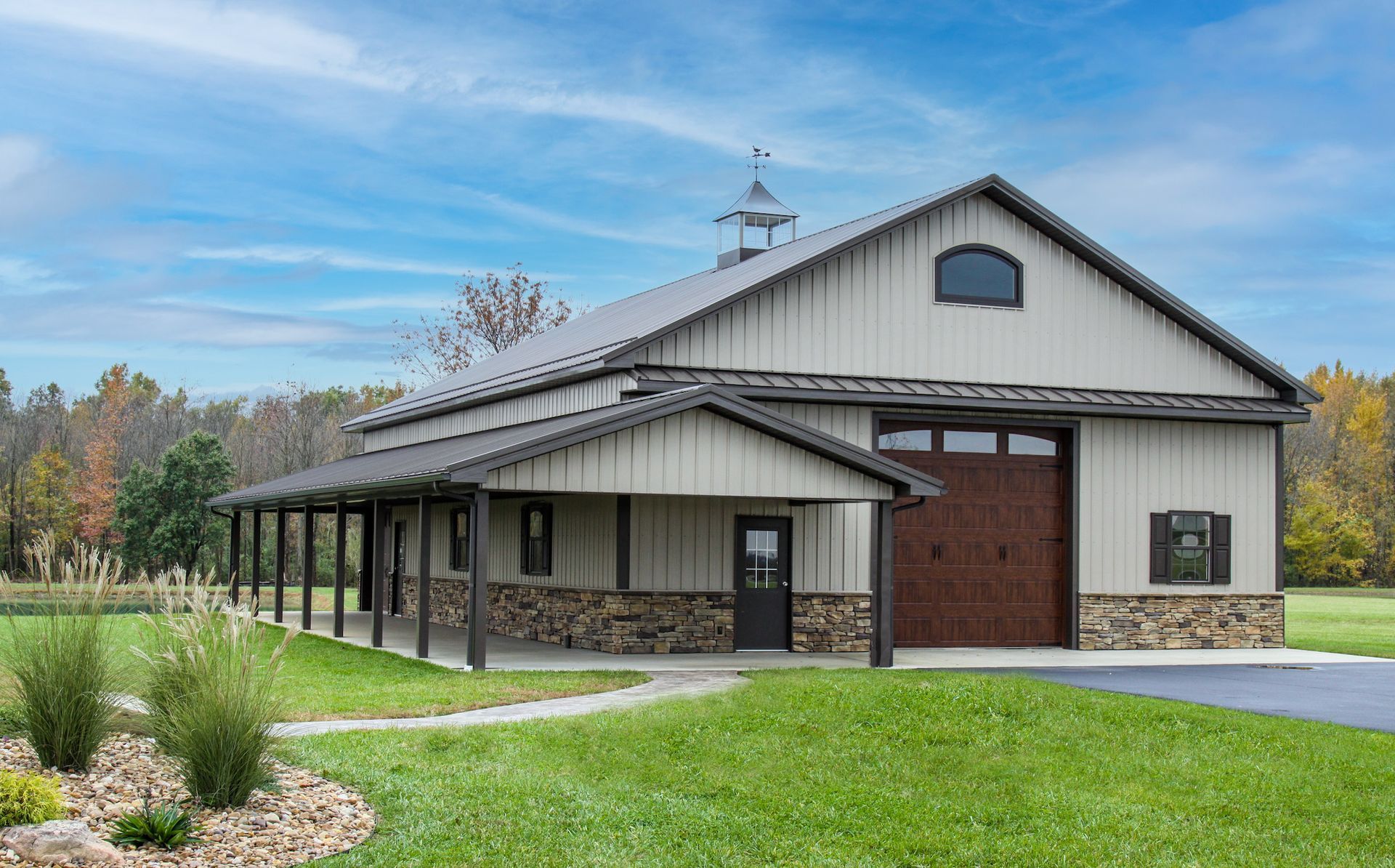 Modern beige building with a covered porch, stone accents, and green lawn under a blue sky